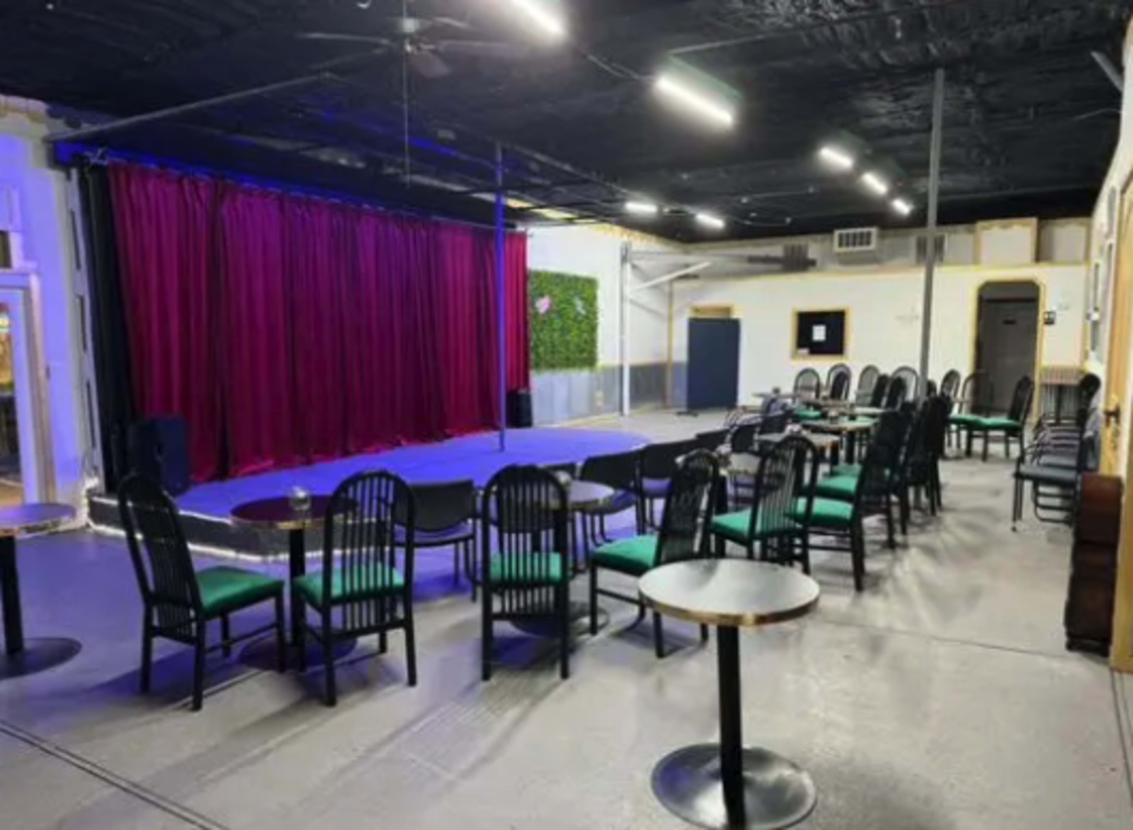 A performance space featuring a stage with purple curtains, surrounded by rows of chairs and tables.