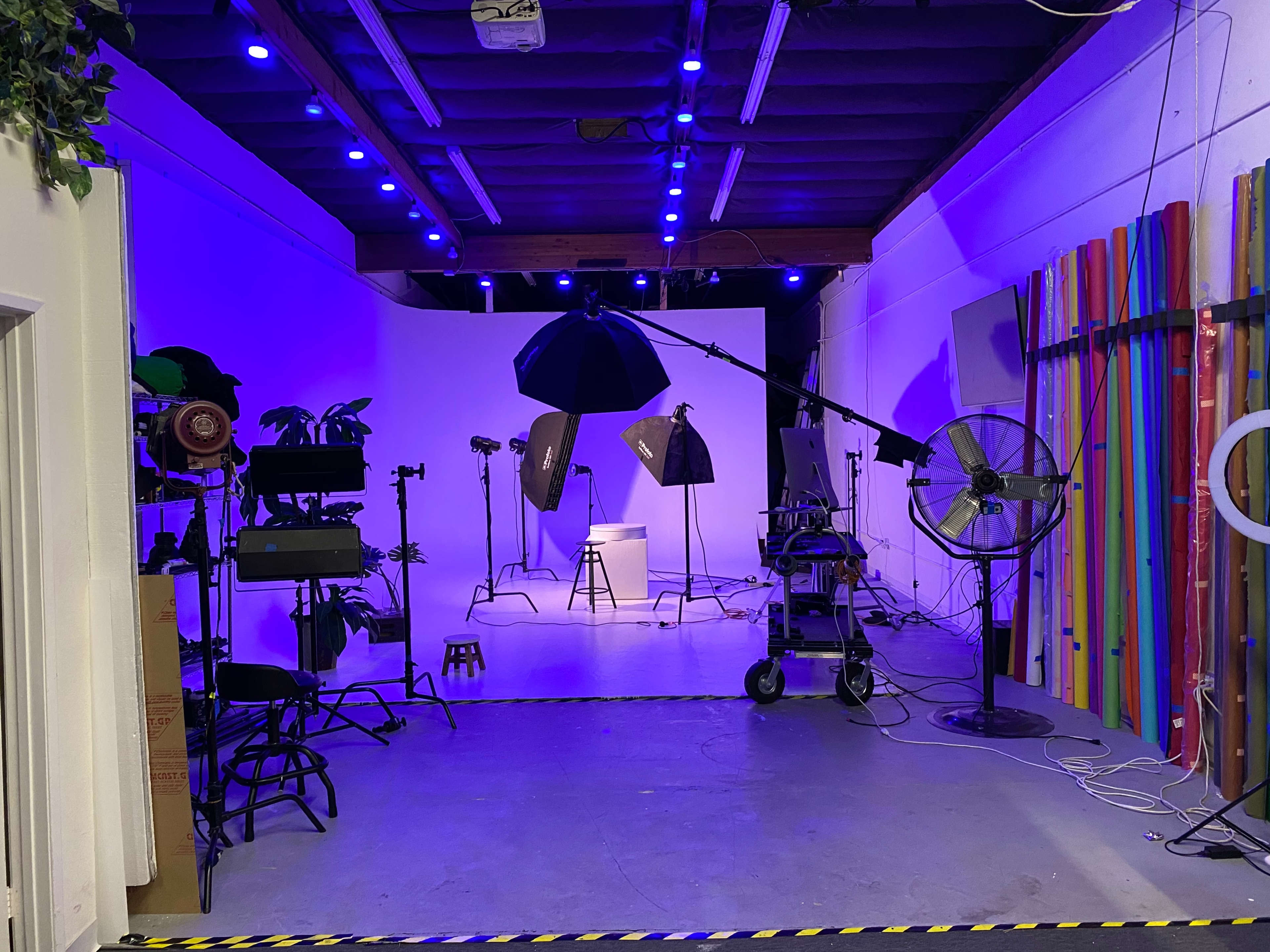 A photography studio is set up with lighting equipment, backdrops, and various props in a room with purple lighting.