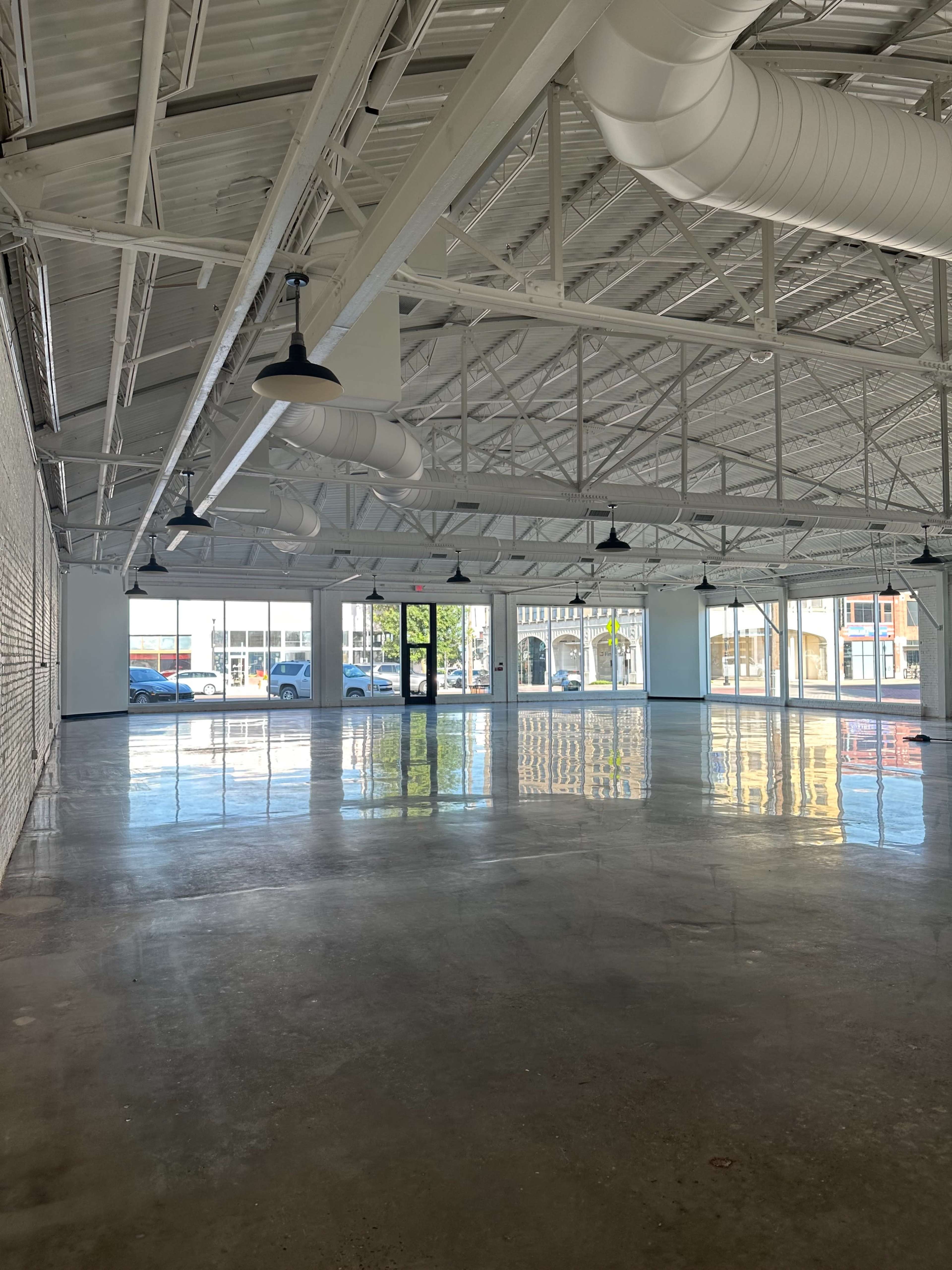 A spacious, empty interior of a building with polished concrete floors and large windows providing natural light.