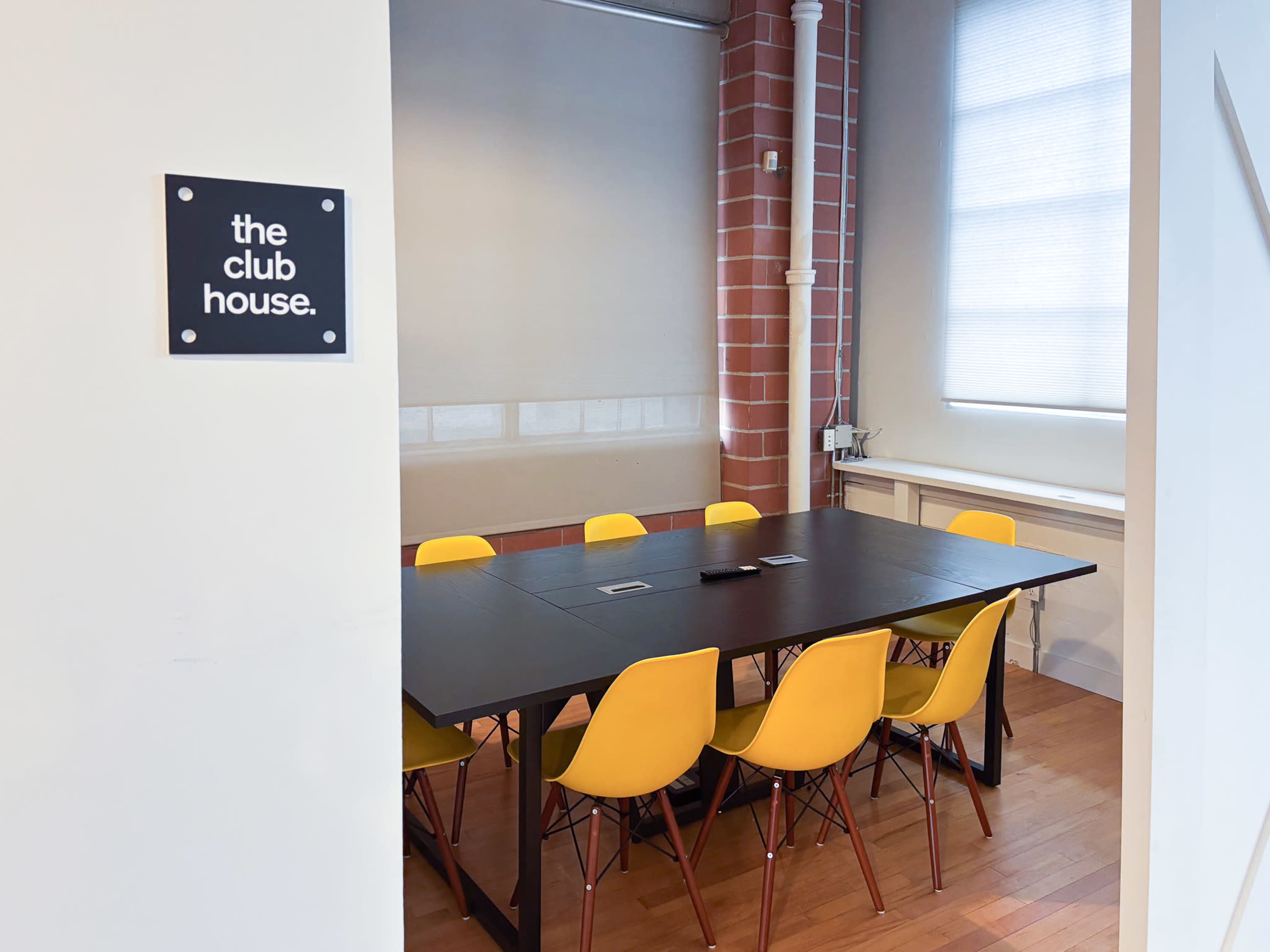 A meeting room with a black table surrounded by yellow chairs is visible, with a sign that reads "the club house" on the wall.
