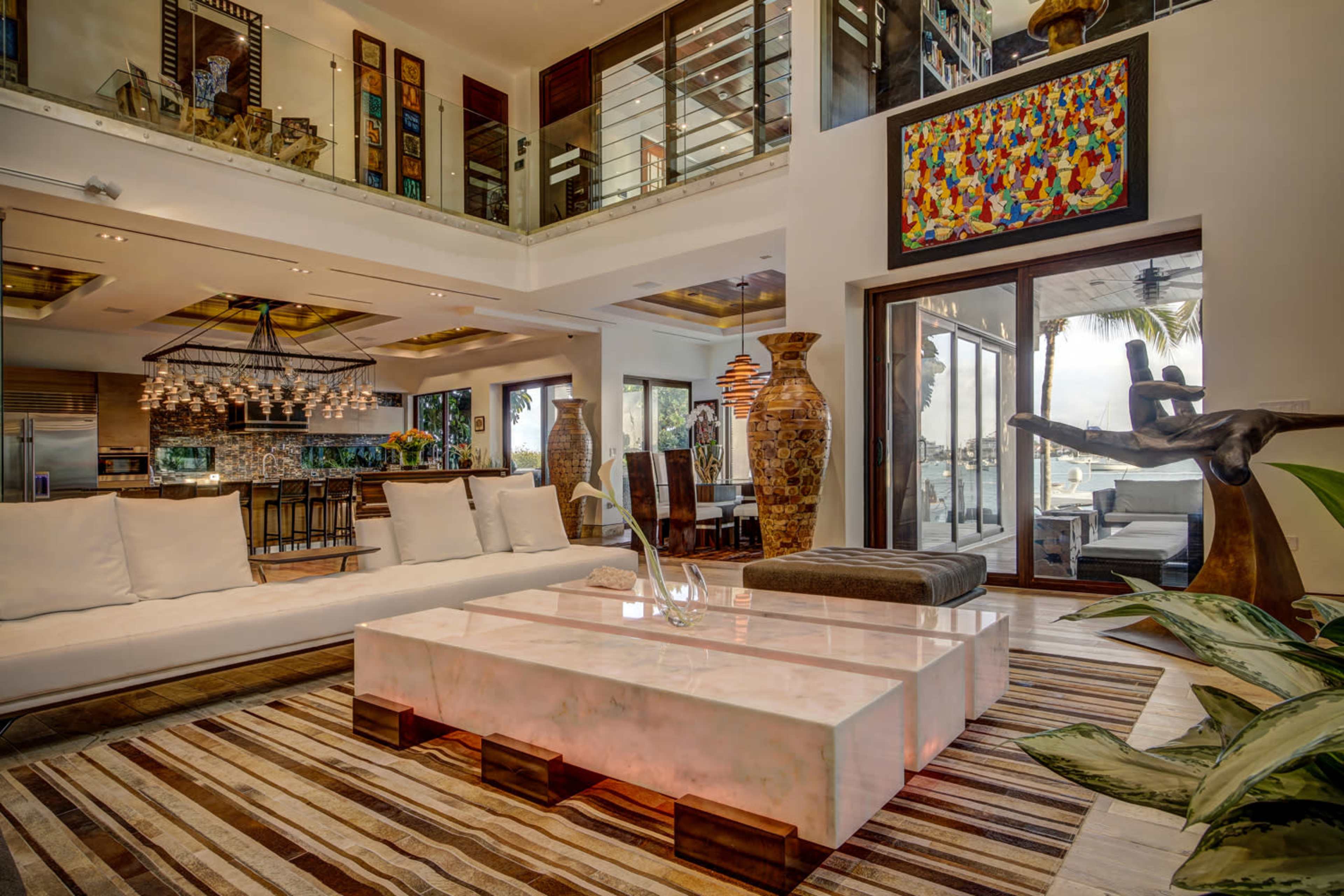 The image shows a modern living space featuring a white sectional sofa, an illuminated coffee table, and a large window overlooking a scenic view.