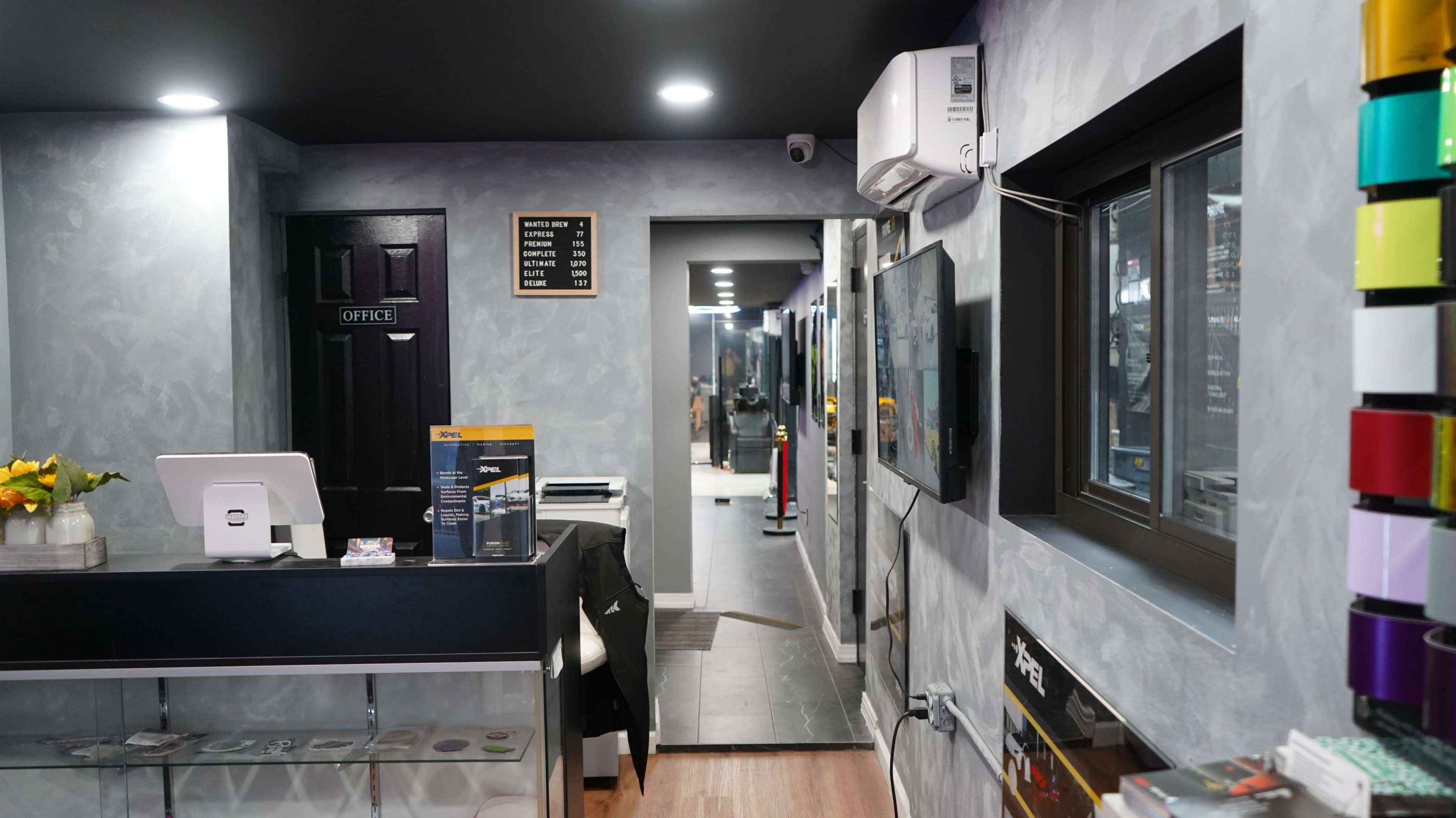 The image shows the interior of a modern office or reception area with a front desk, gray walls, and a hallway leading to additional spaces.