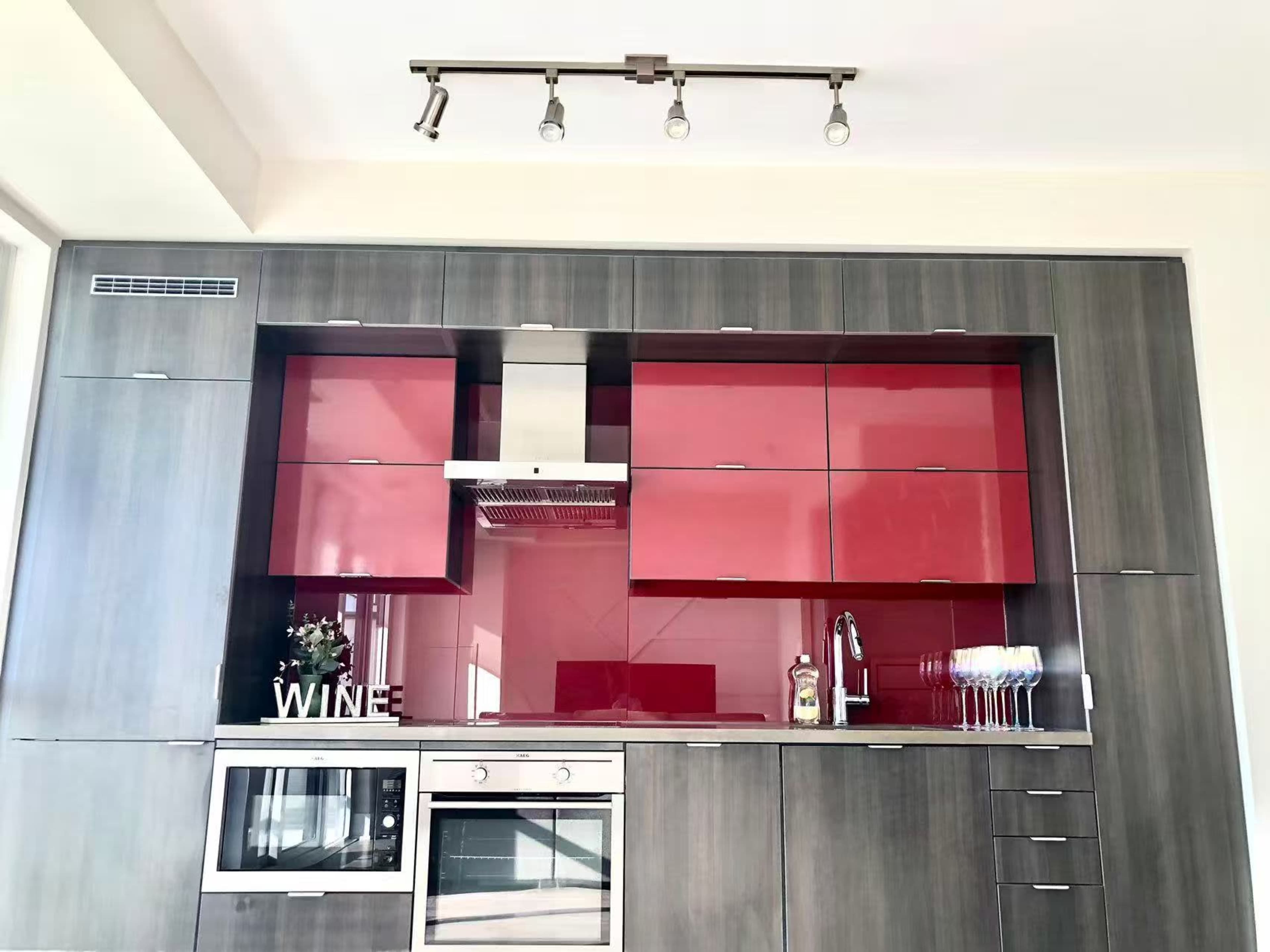 The image shows a modern kitchen with gray cabinetry, red glass upper cabinets, and stainless steel appliances.