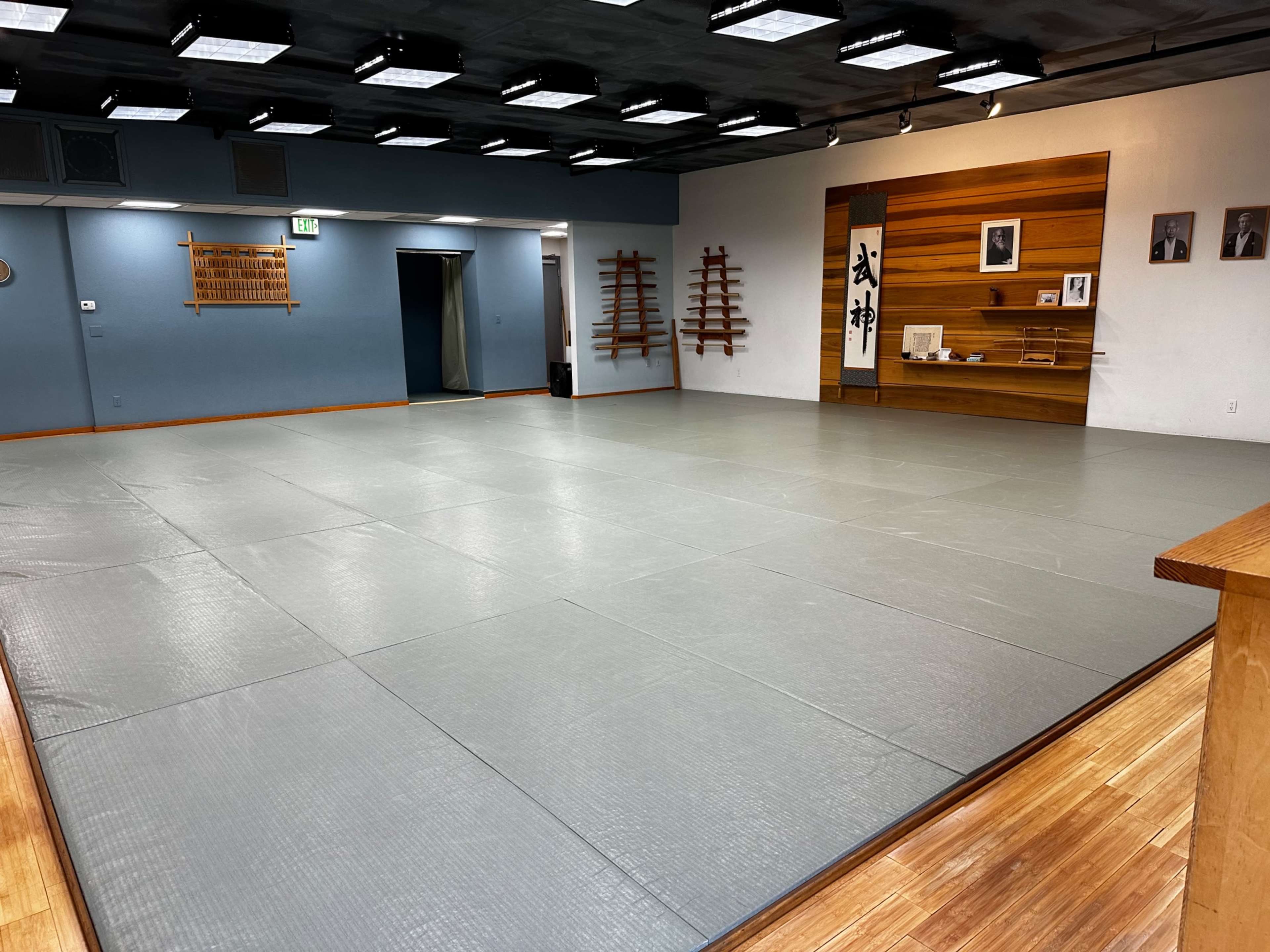 A spacious martial arts dojo with grey mats and wooden accents on the walls.