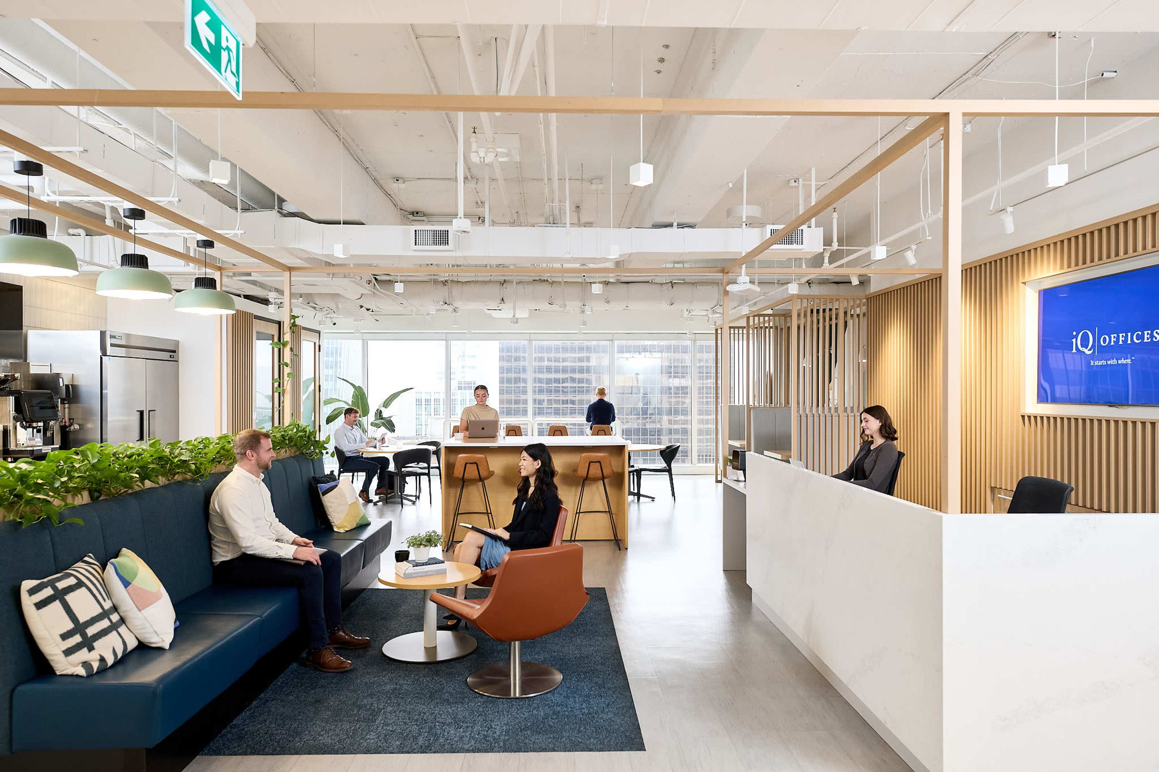 The image shows a modern office space with a reception area, seating arrangements, and people working at a communal table.