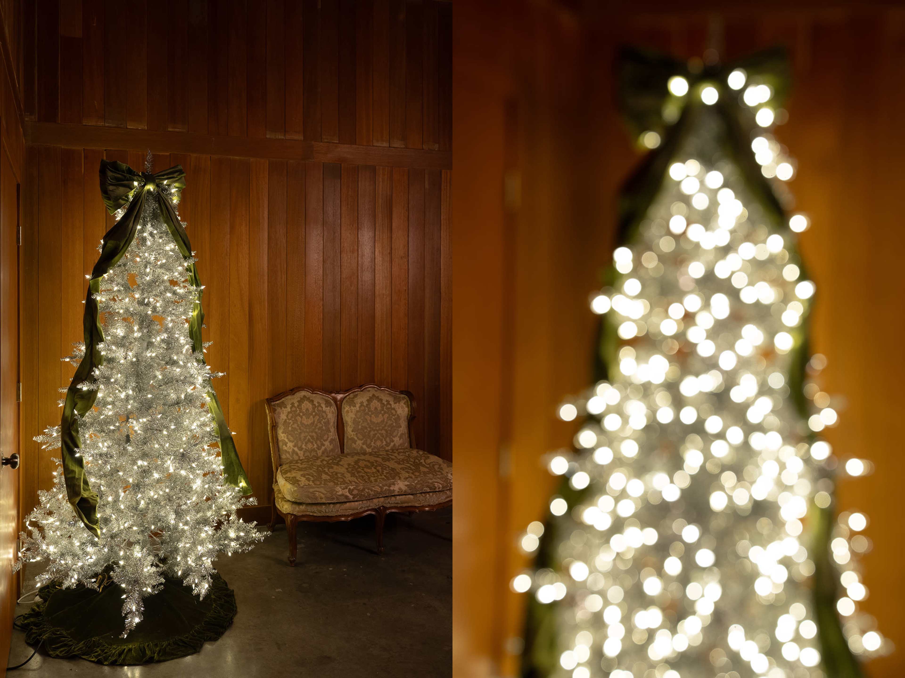 A decorated Christmas tree with white lights stands next to a vintage couch in a wooden-paneled room.