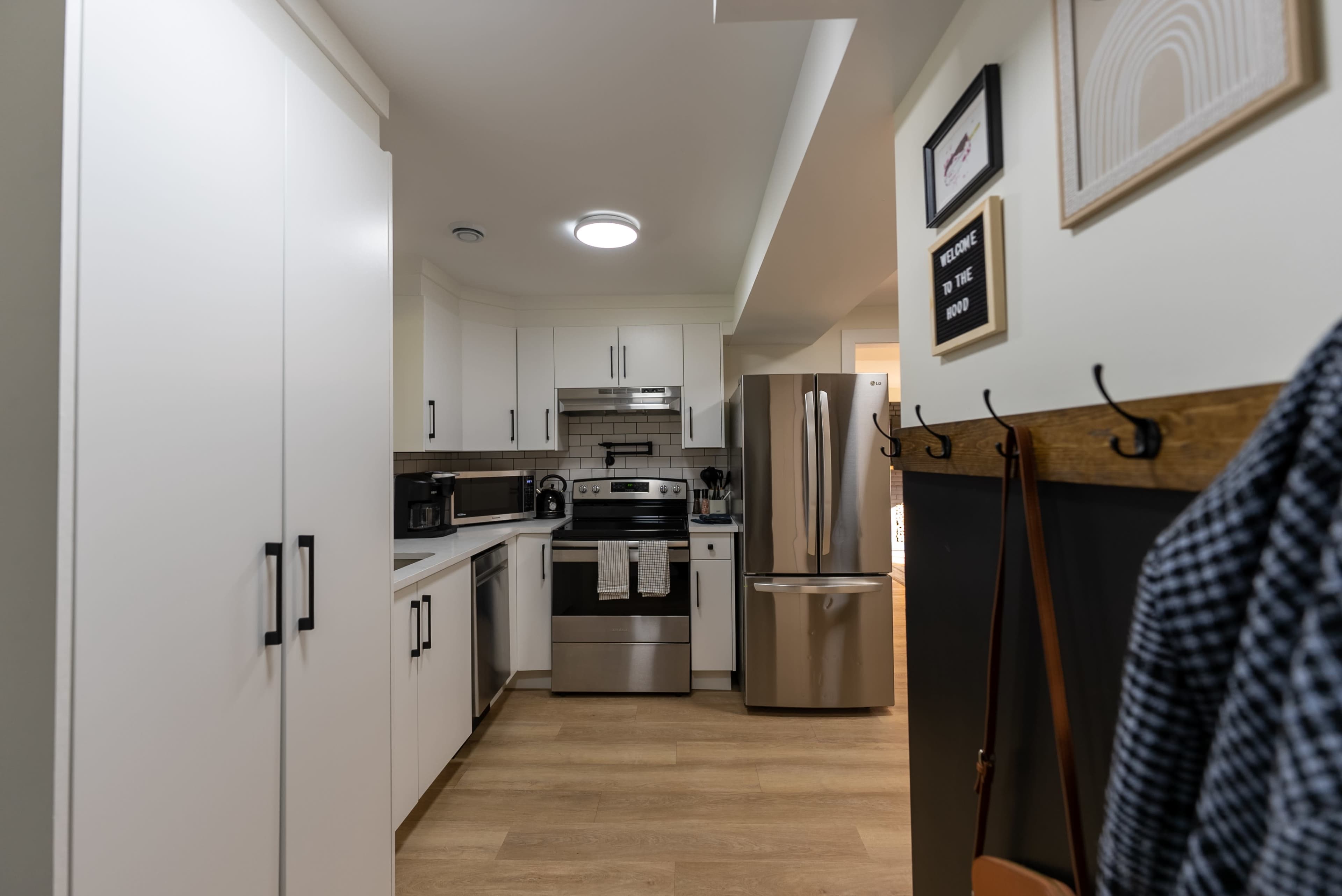 A modern kitchen with white cabinets, stainless steel appliances, and light wood flooring.