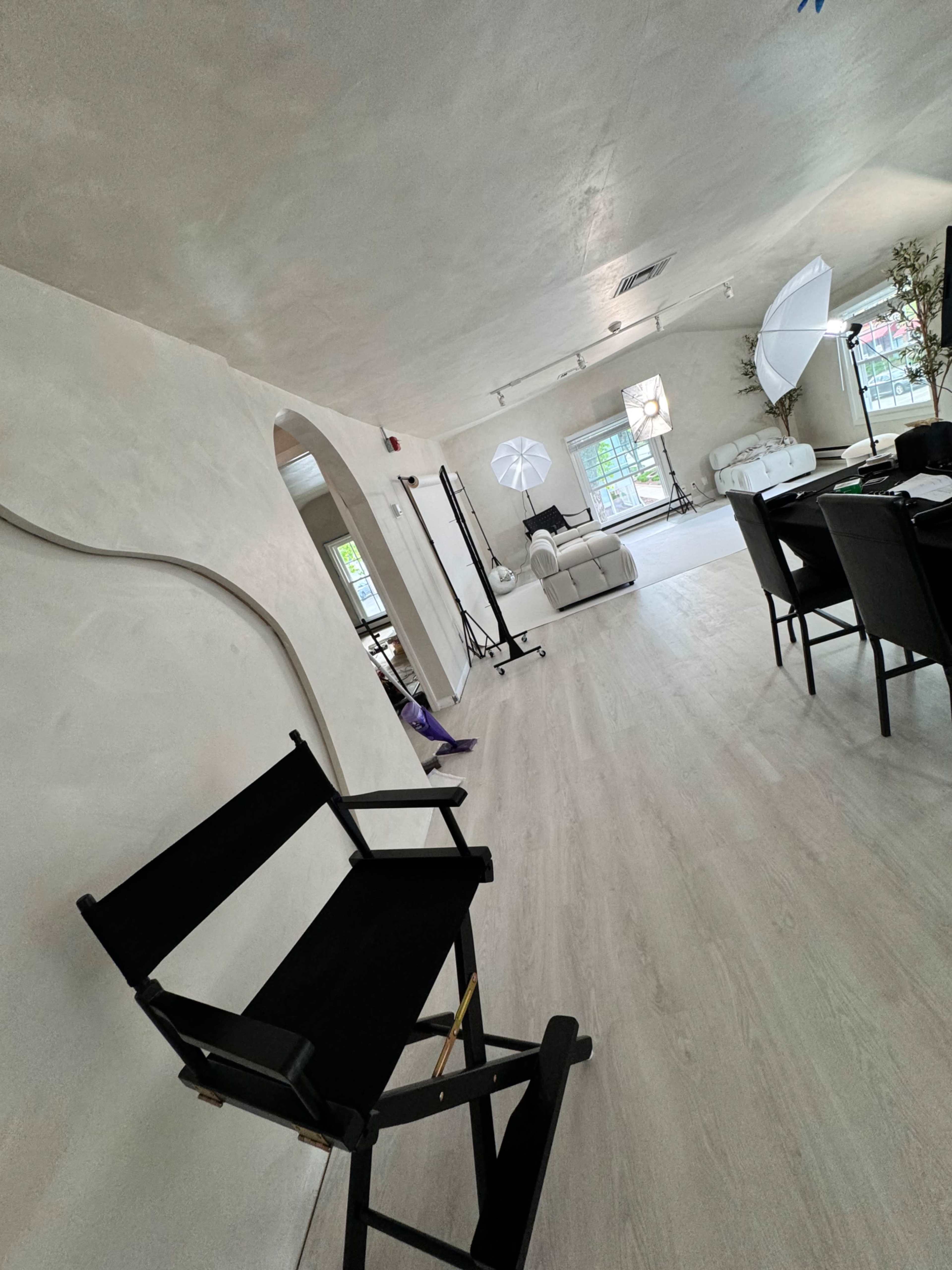 A bright, spacious interior with a director's chair in the foreground and photography equipment scattered throughout the room.
