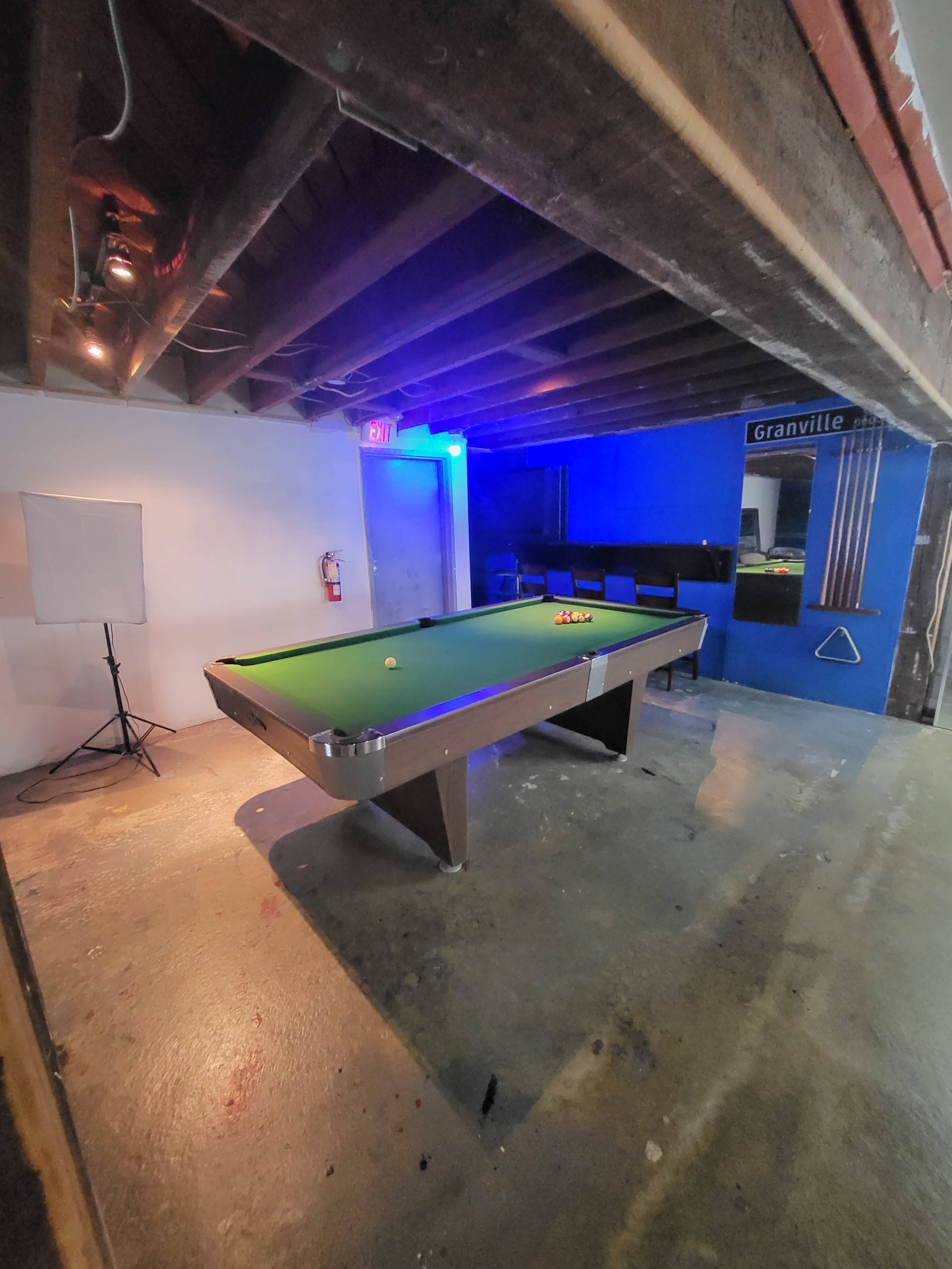 A pool table in a basement or recreational area, with blue lighting and a wall labeled "Granville."