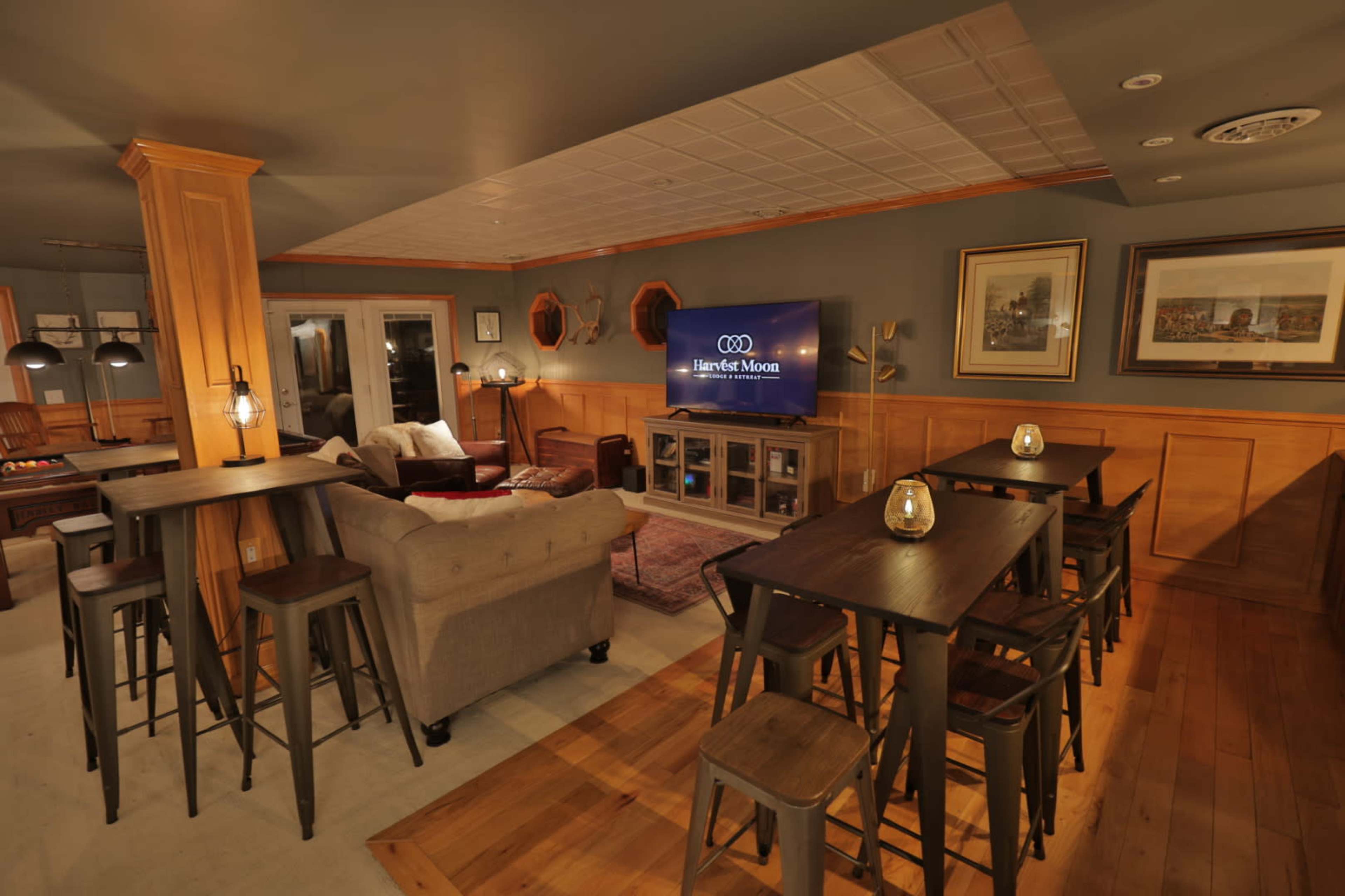 A cozy lounge area featuring a comfortable seating arrangement, wooden bar tables, and a large TV mounted on the wall.