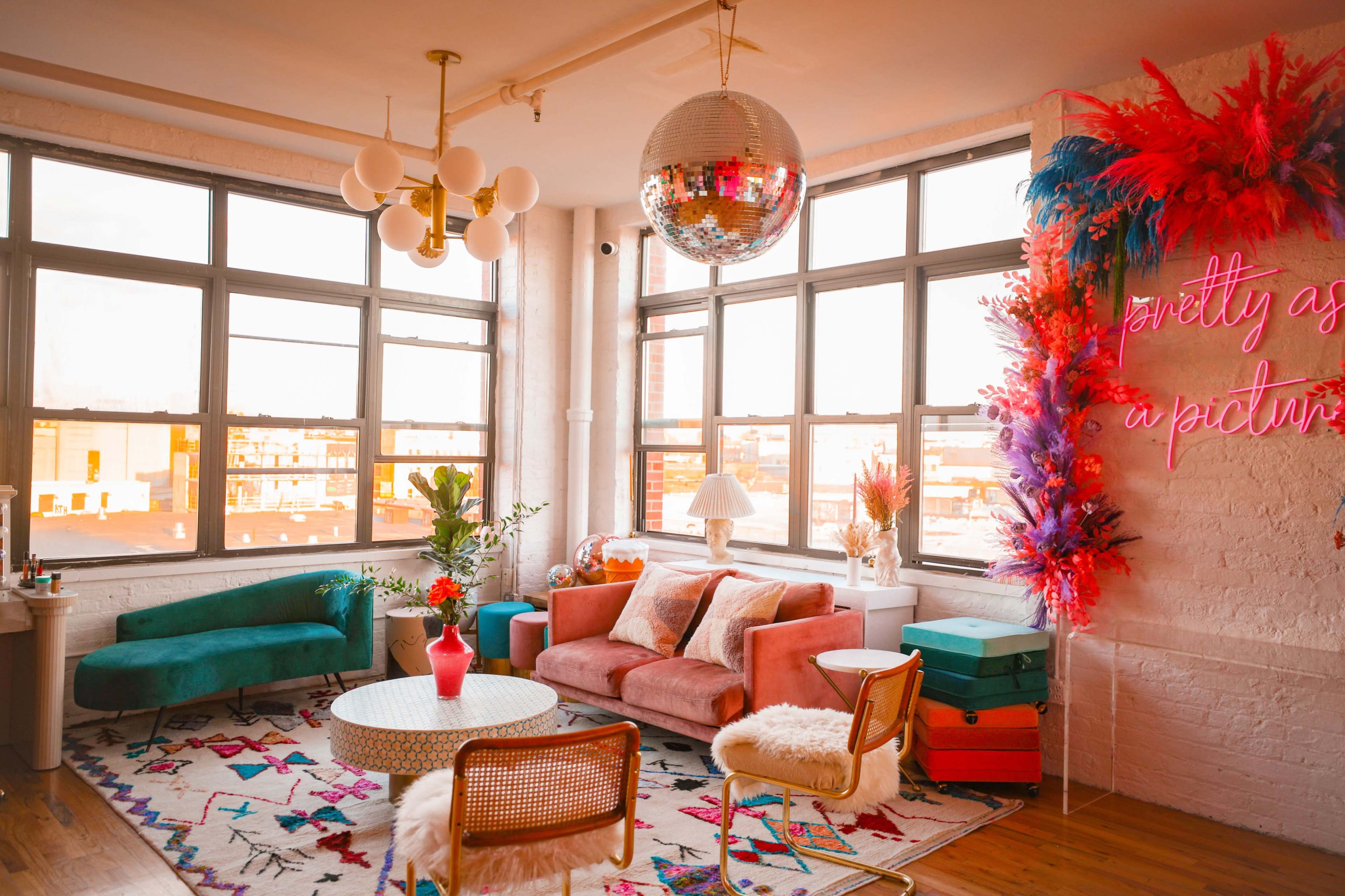 The image shows a brightly lit living room with large windows, colorful furniture, a disco ball, and decorative plants.