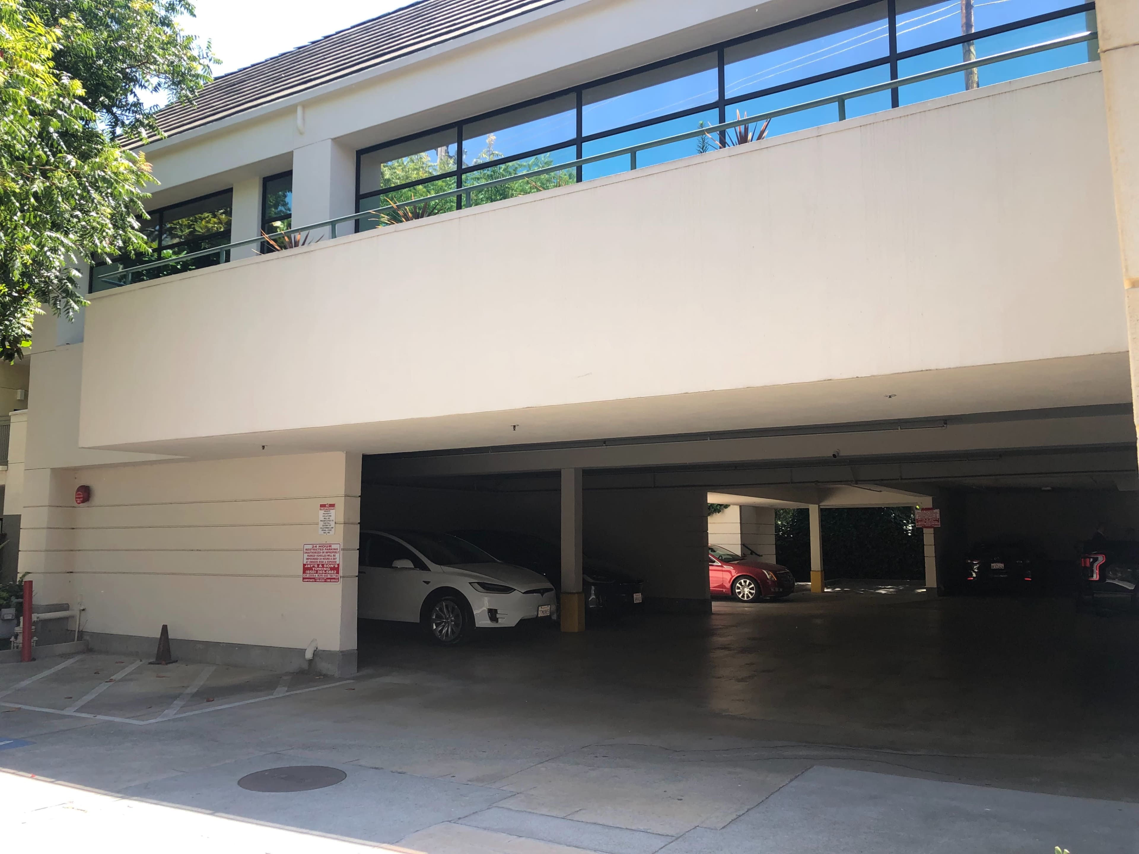The image shows a multi-level parking structure with a white car parked on the left side and a red car in the back.