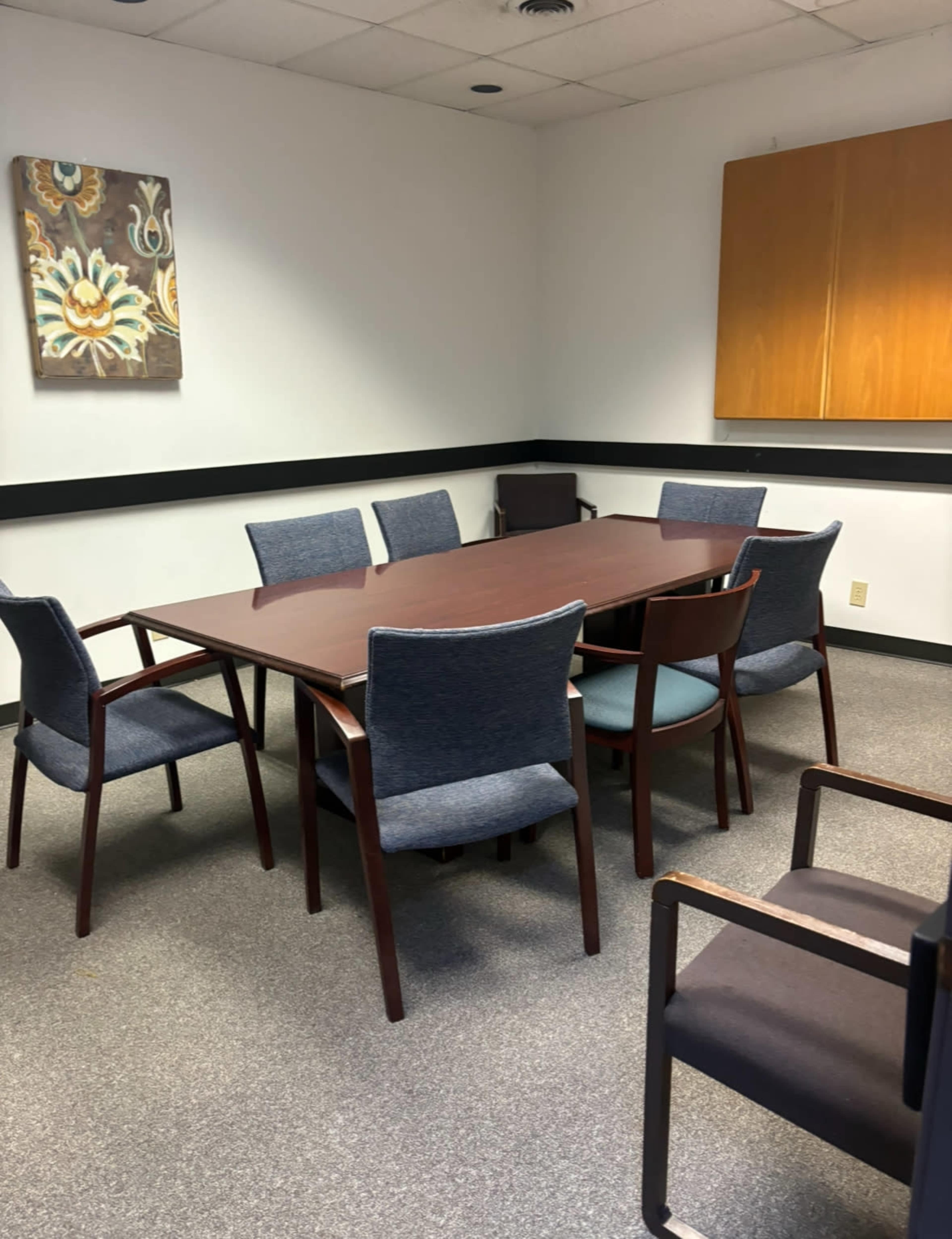 A conference room features a large wooden table surrounded by several chairs and a wall-mounted cabinet.