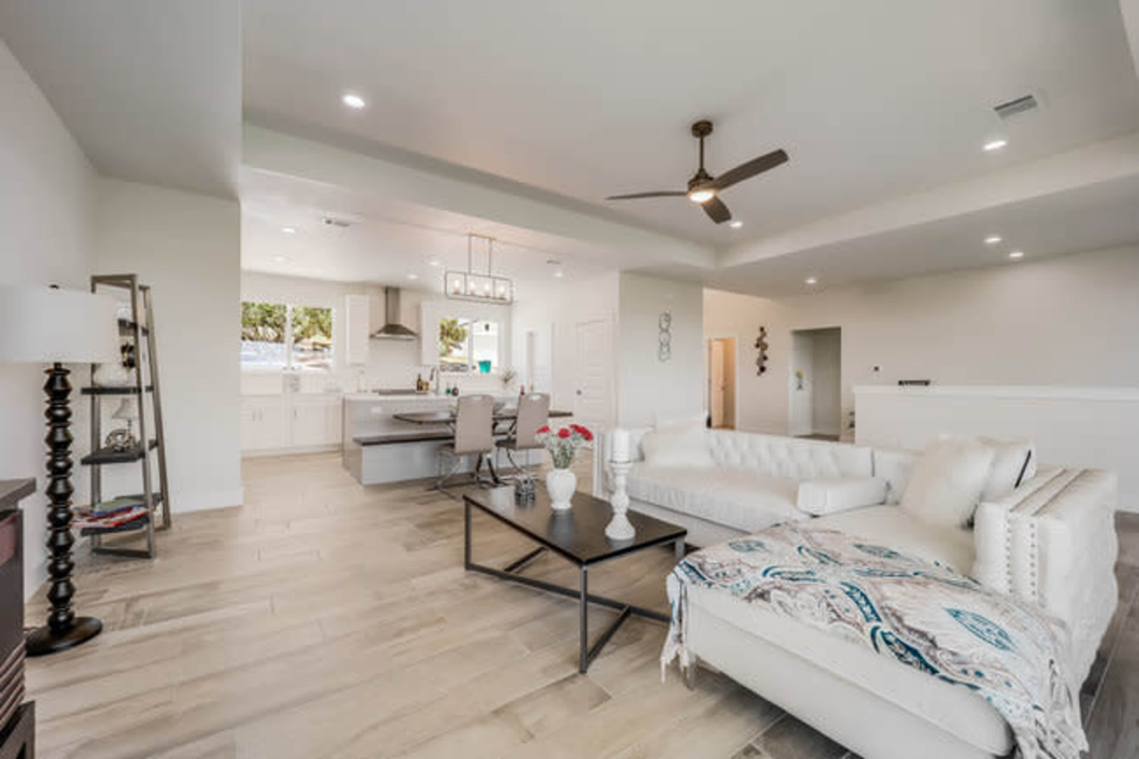 The image shows a modern living room with a white sectional sofa, a dark coffee table, and a kitchen area visible in the background.