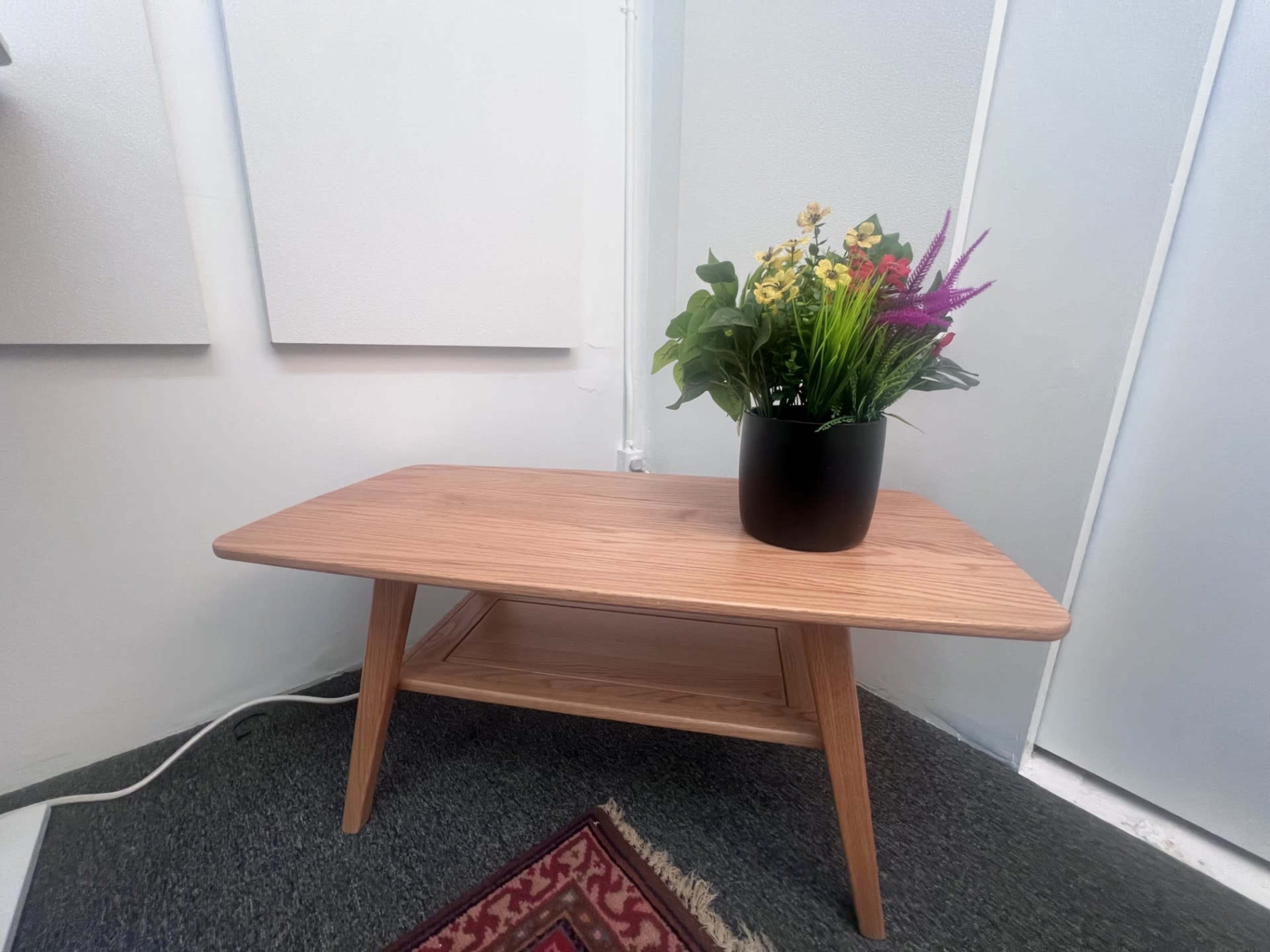A wooden coffee table with a tapered design holds a potted arrangement of colorful flowers.