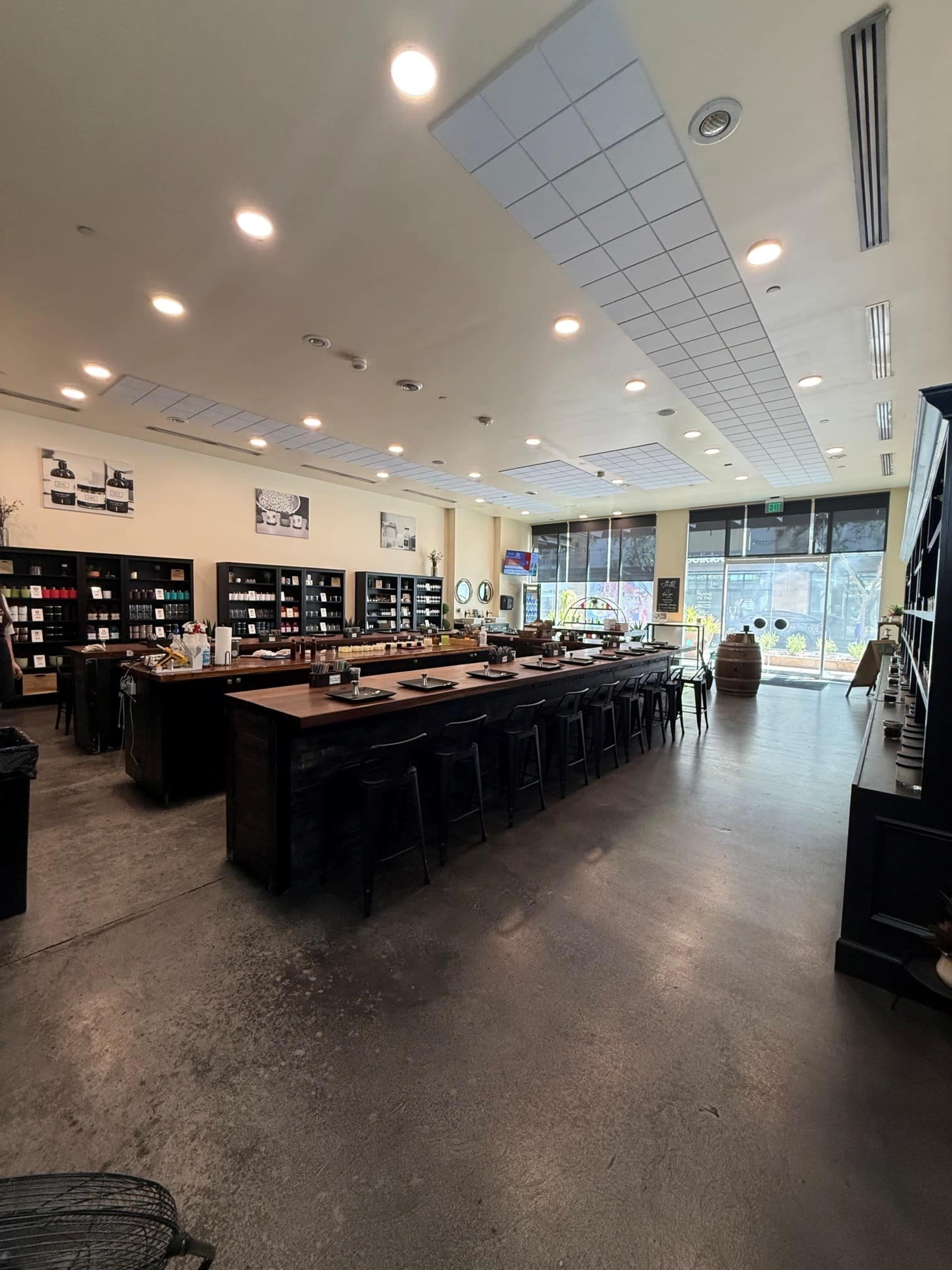 The image shows a spacious café interior with a long counter, shelves lined with various items, and large windows allowing natural light to enter.
