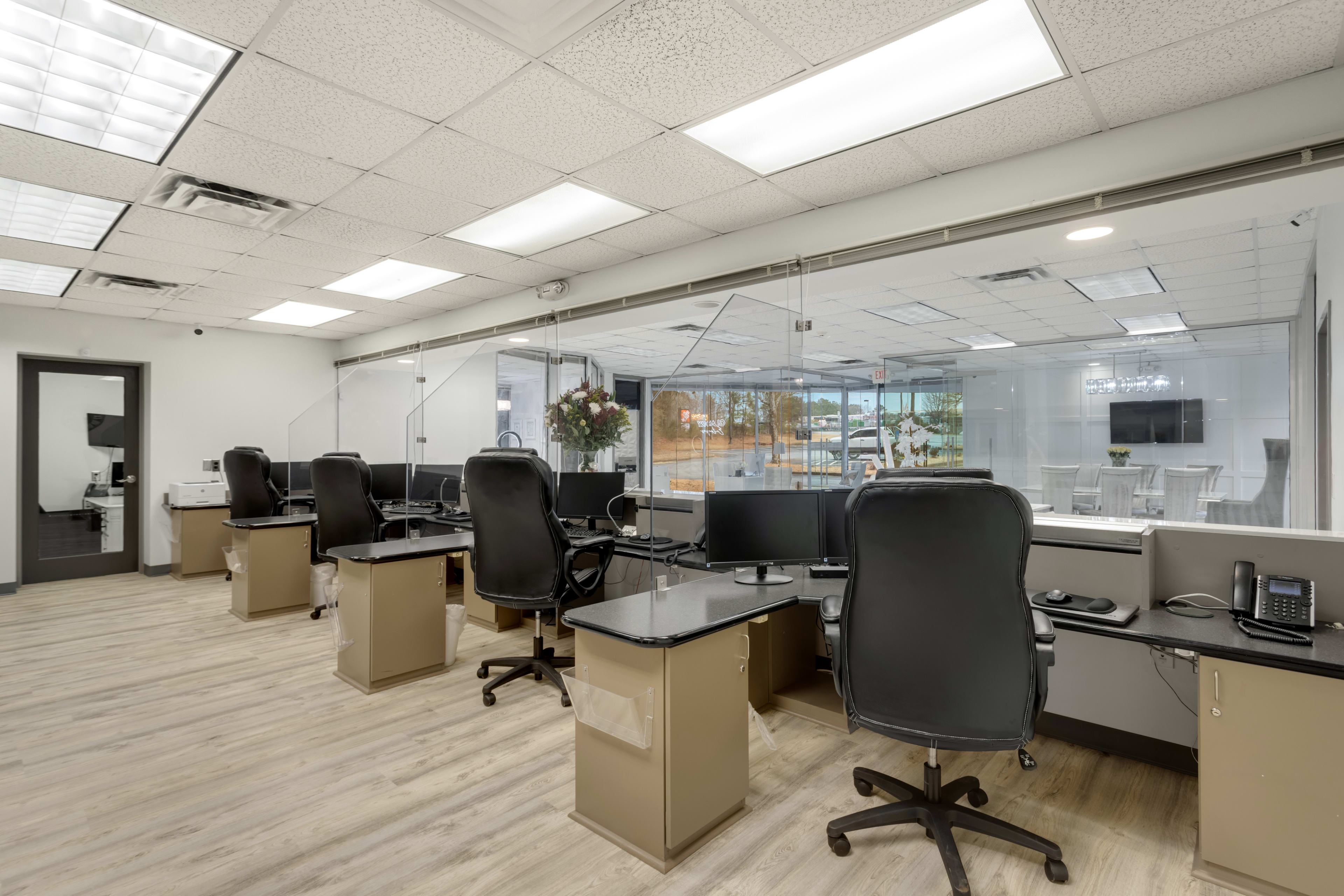 A modern office space with several workstations featuring desks, chairs, and partitioned acrylic dividers.