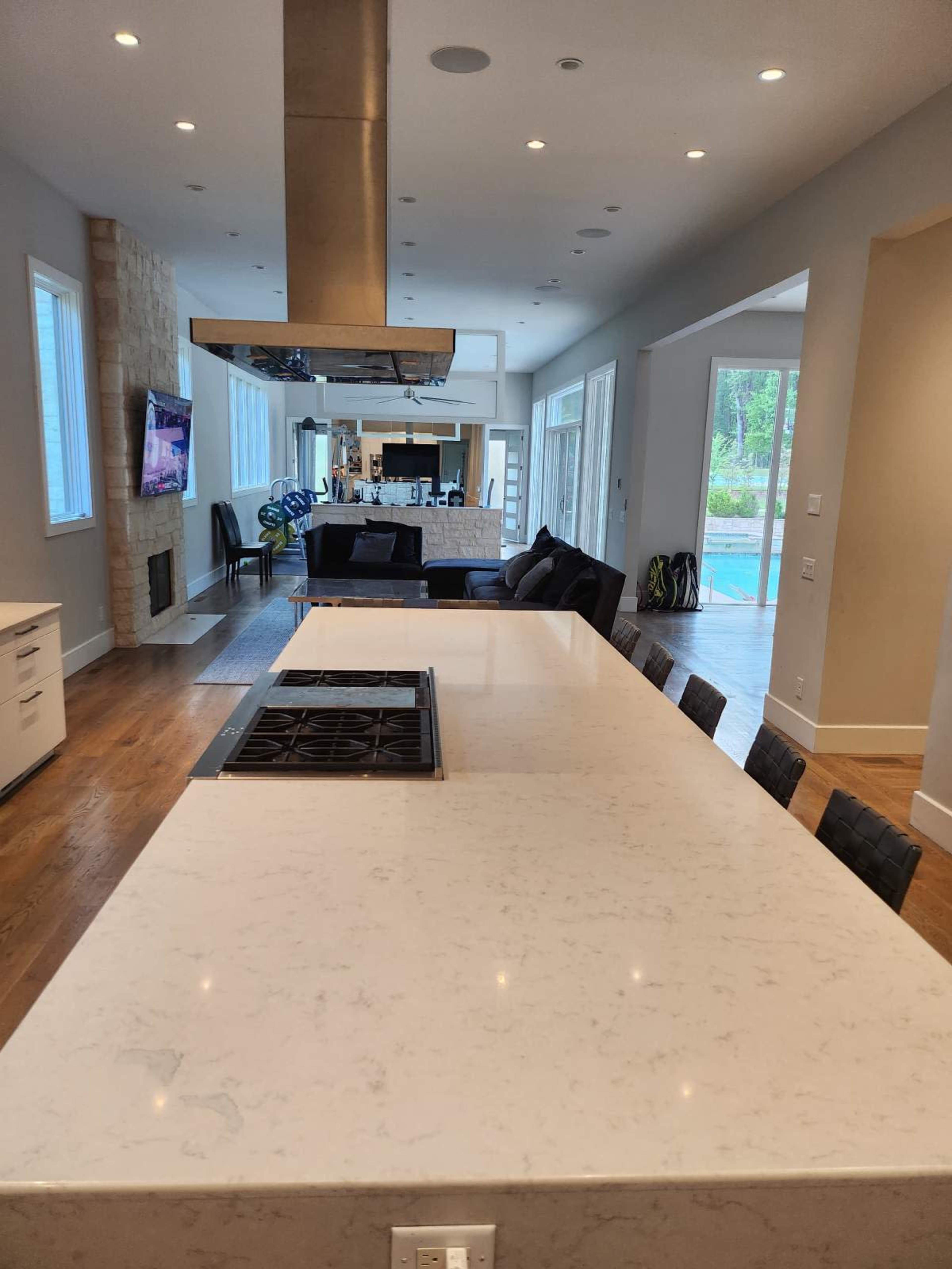 A modern kitchen with a large marble countertop, a gas stovetop, and an open layout leading to a living area with a view of the pool outside.