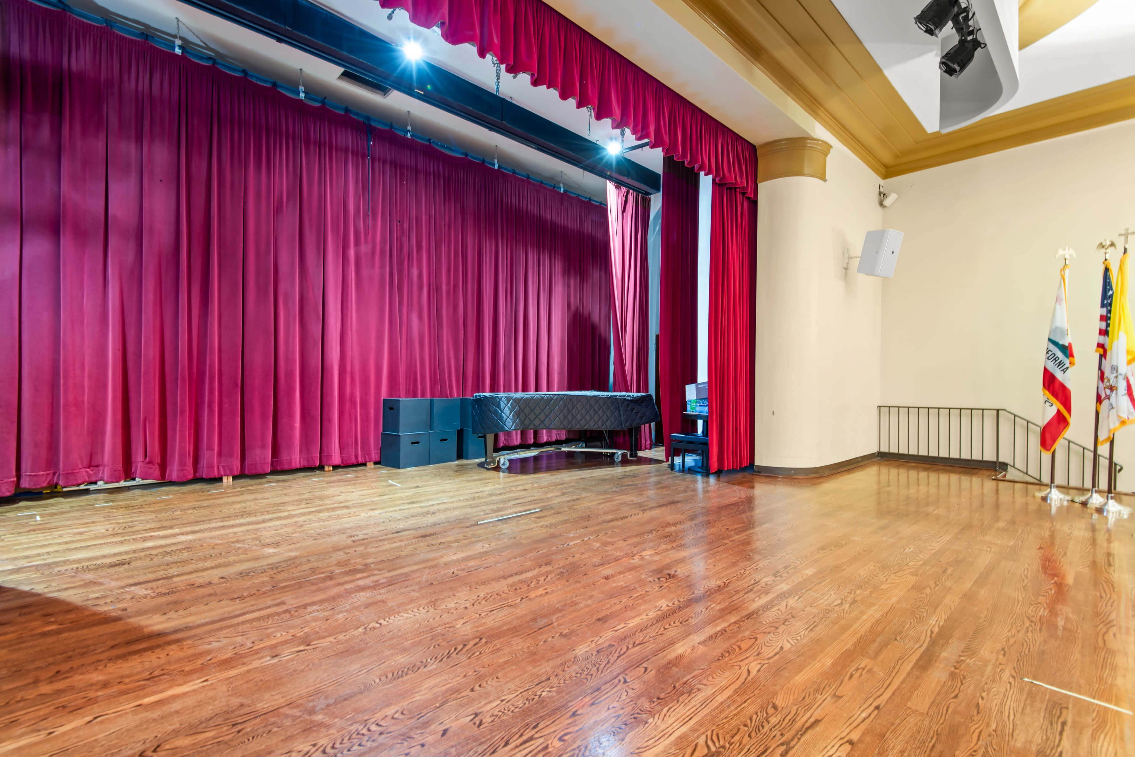 The image shows a stage with red curtains, a black piano, and wooden flooring in a performance hall.