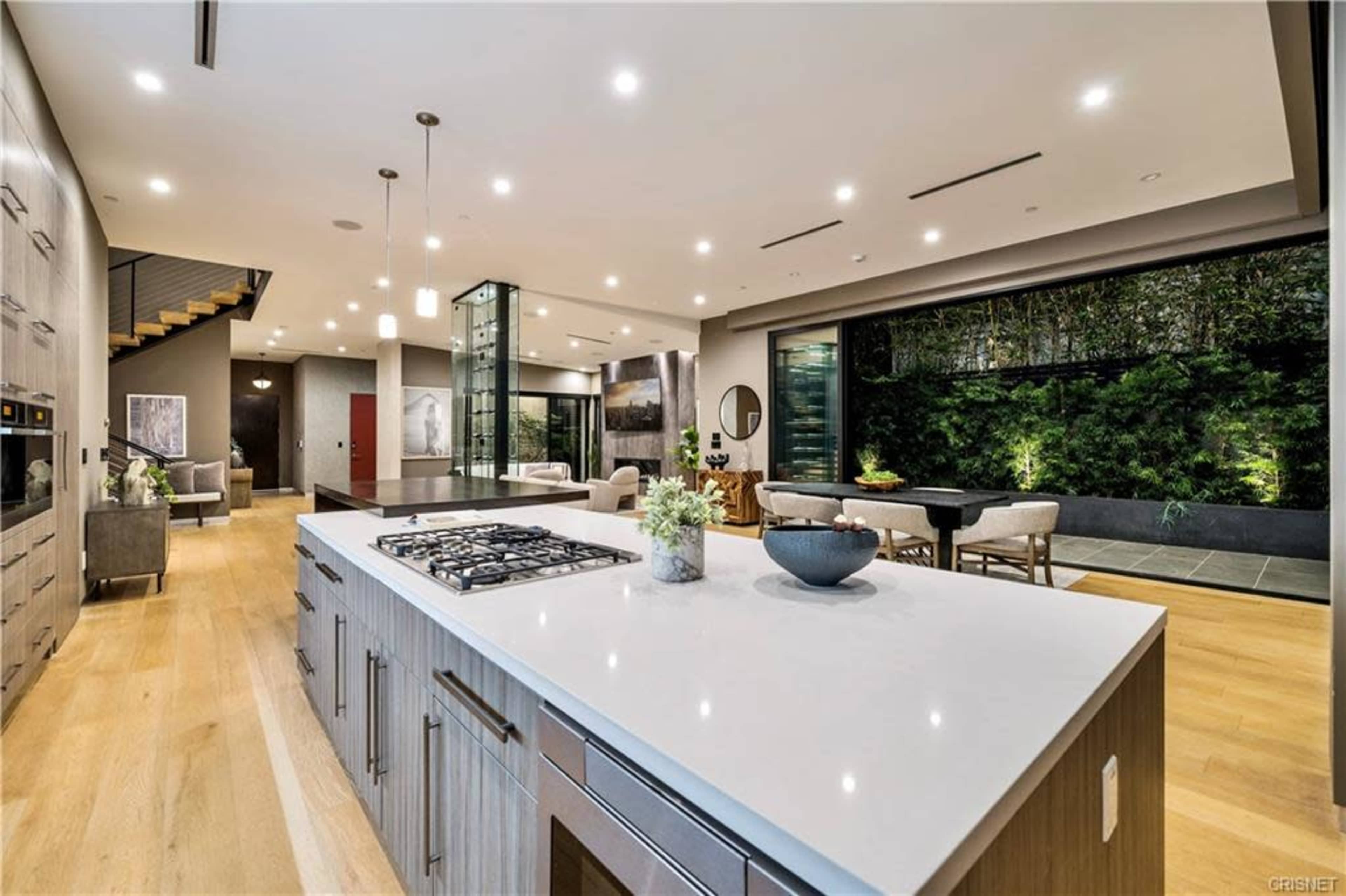 A modern kitchen with a large island, open to a spacious living area that features a dining table and a wall of greenery.