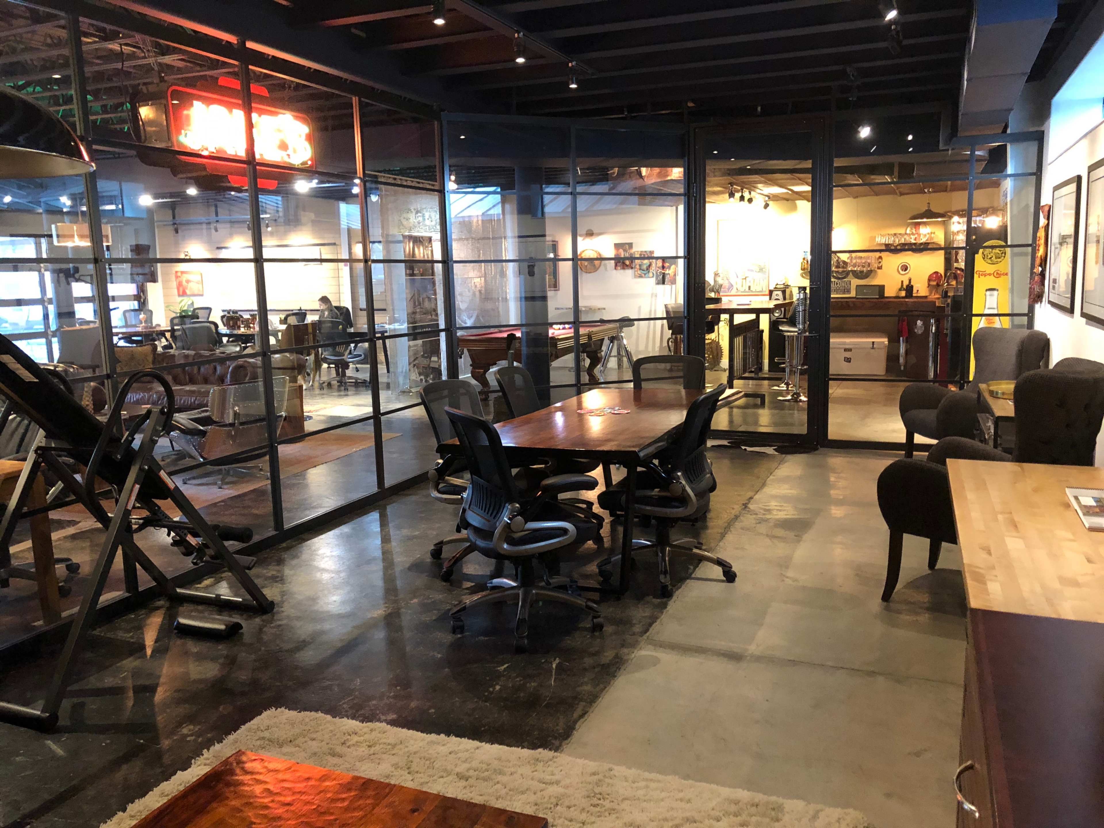 A modern interior features a glass-walled meeting room with a wooden table and black office chairs, adjacent to a cozy lounge area.