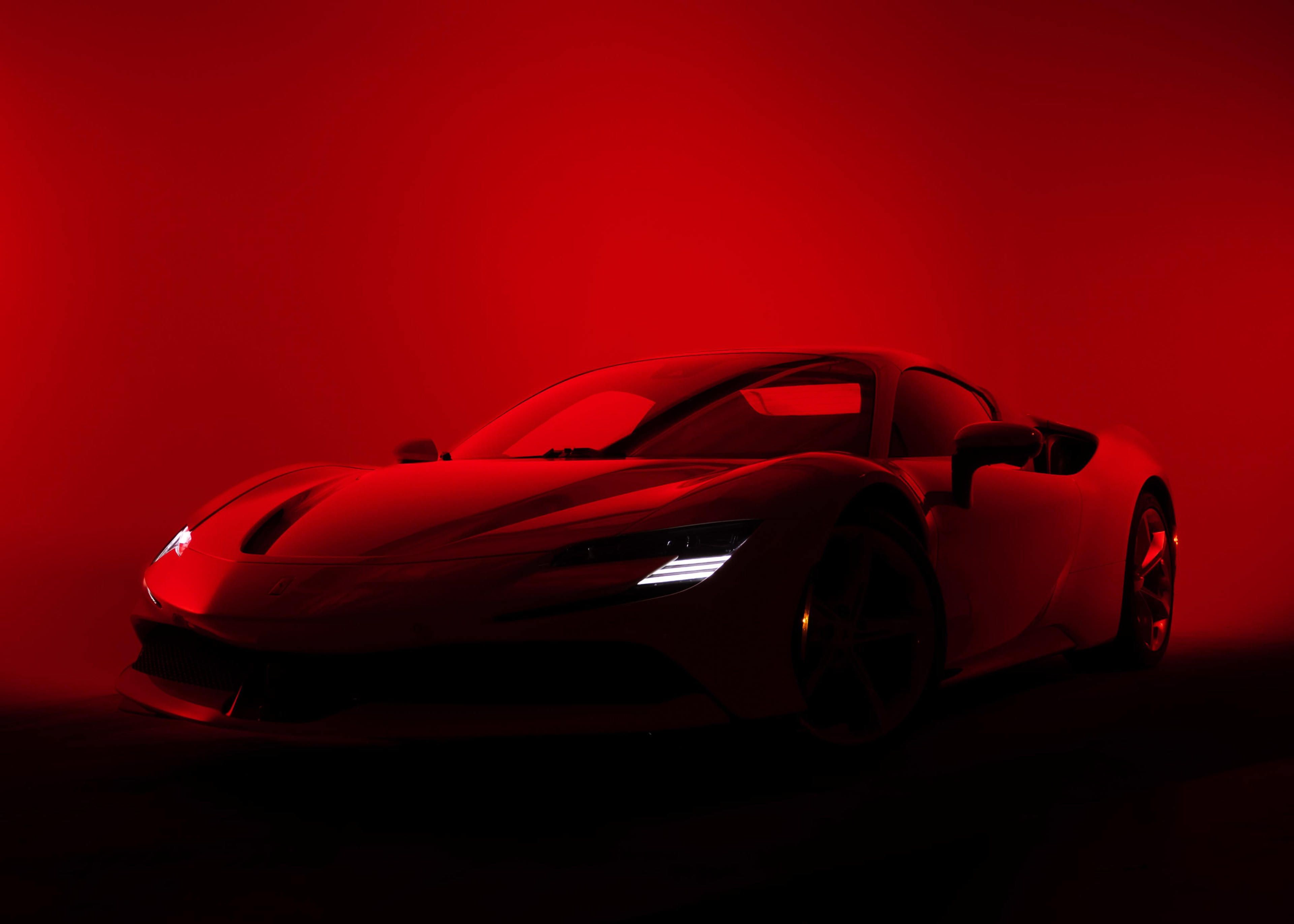 A sleek, white sports car is illuminated by red light against a dark background.