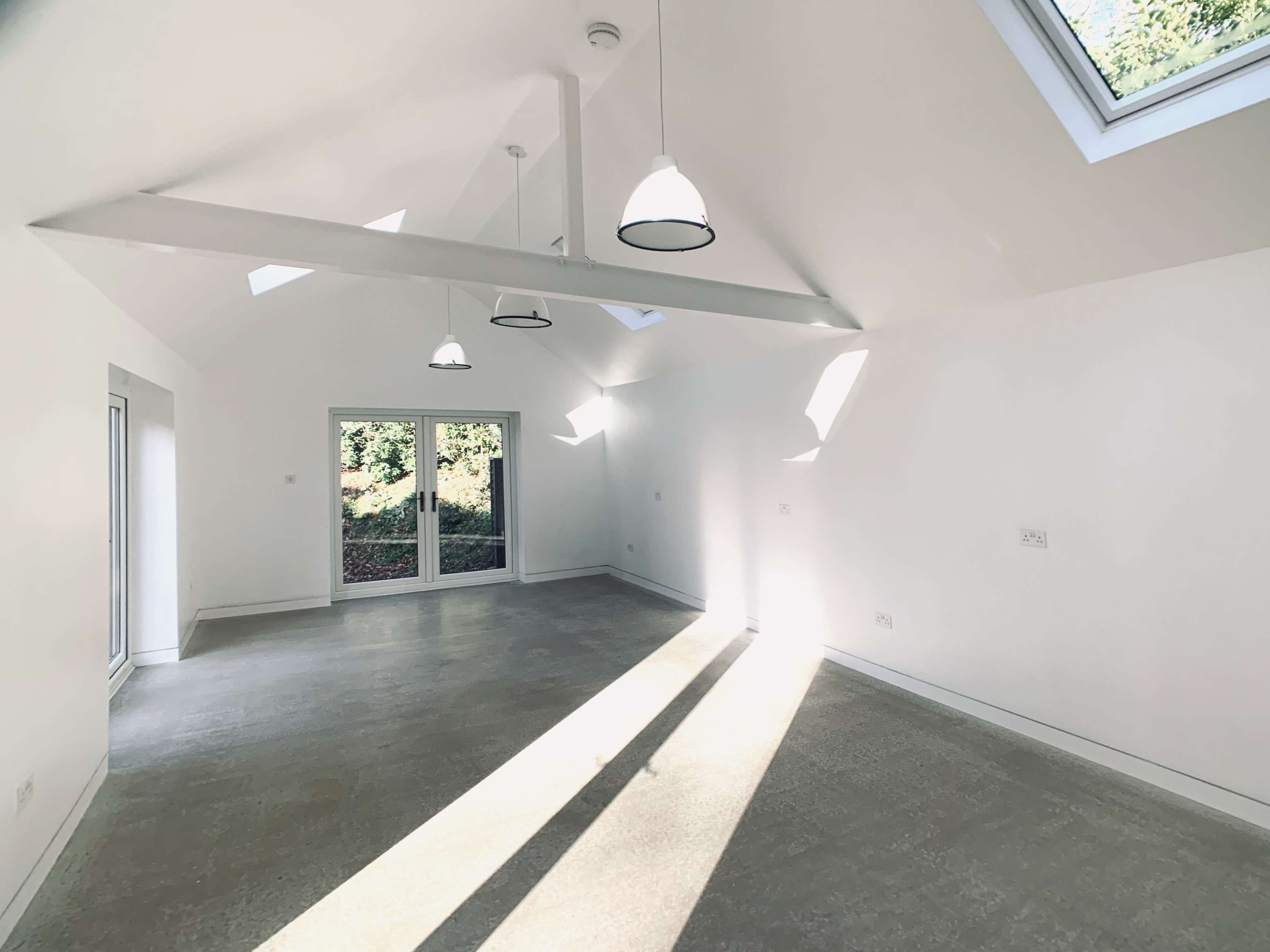 The image shows a spacious, brightly lit room with a vaulted ceiling, featuring large windows and three pendant lights.