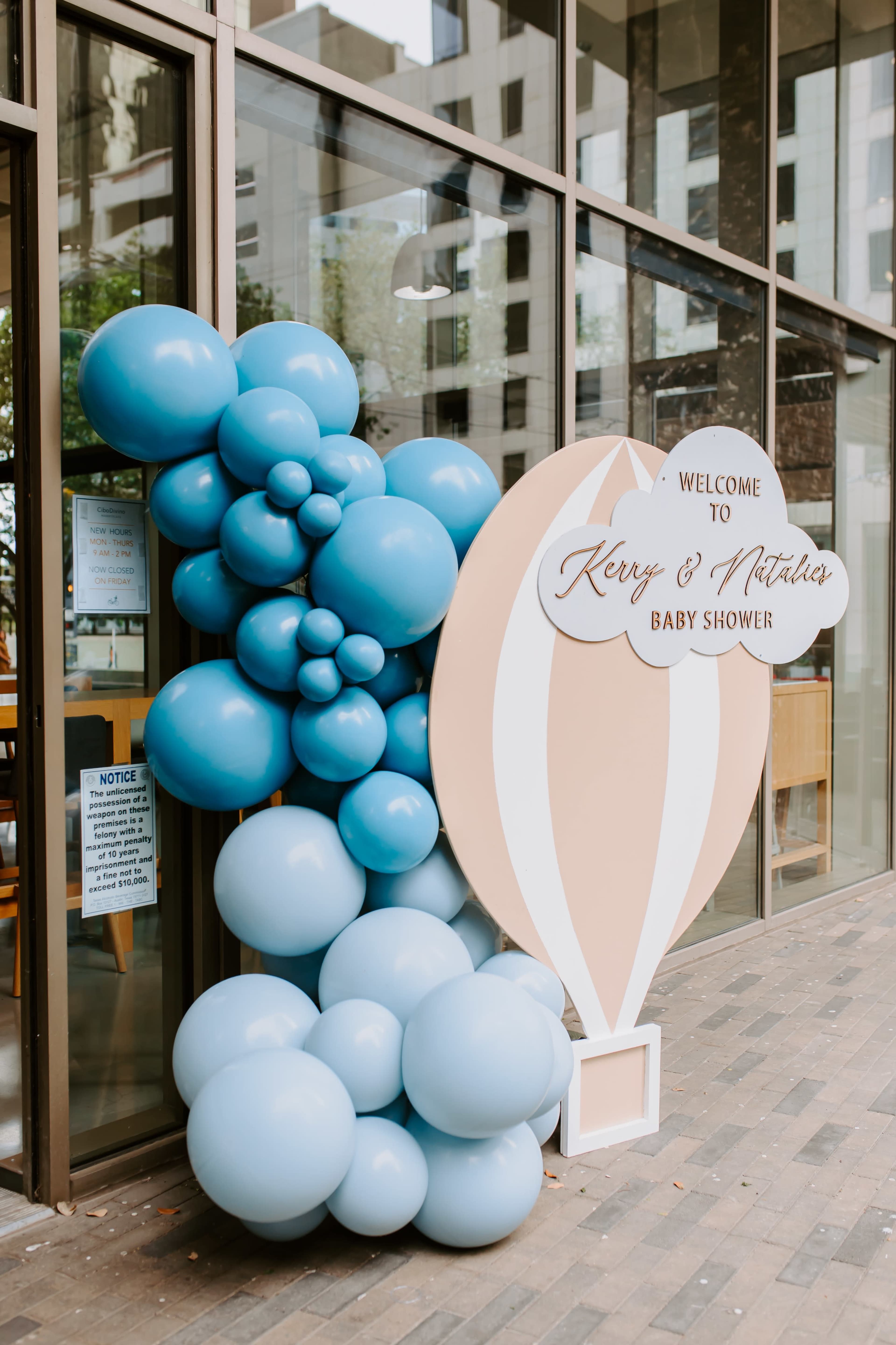 A decorative entrance featuring clusters of blue balloons and a sign welcoming guests to a baby shower.