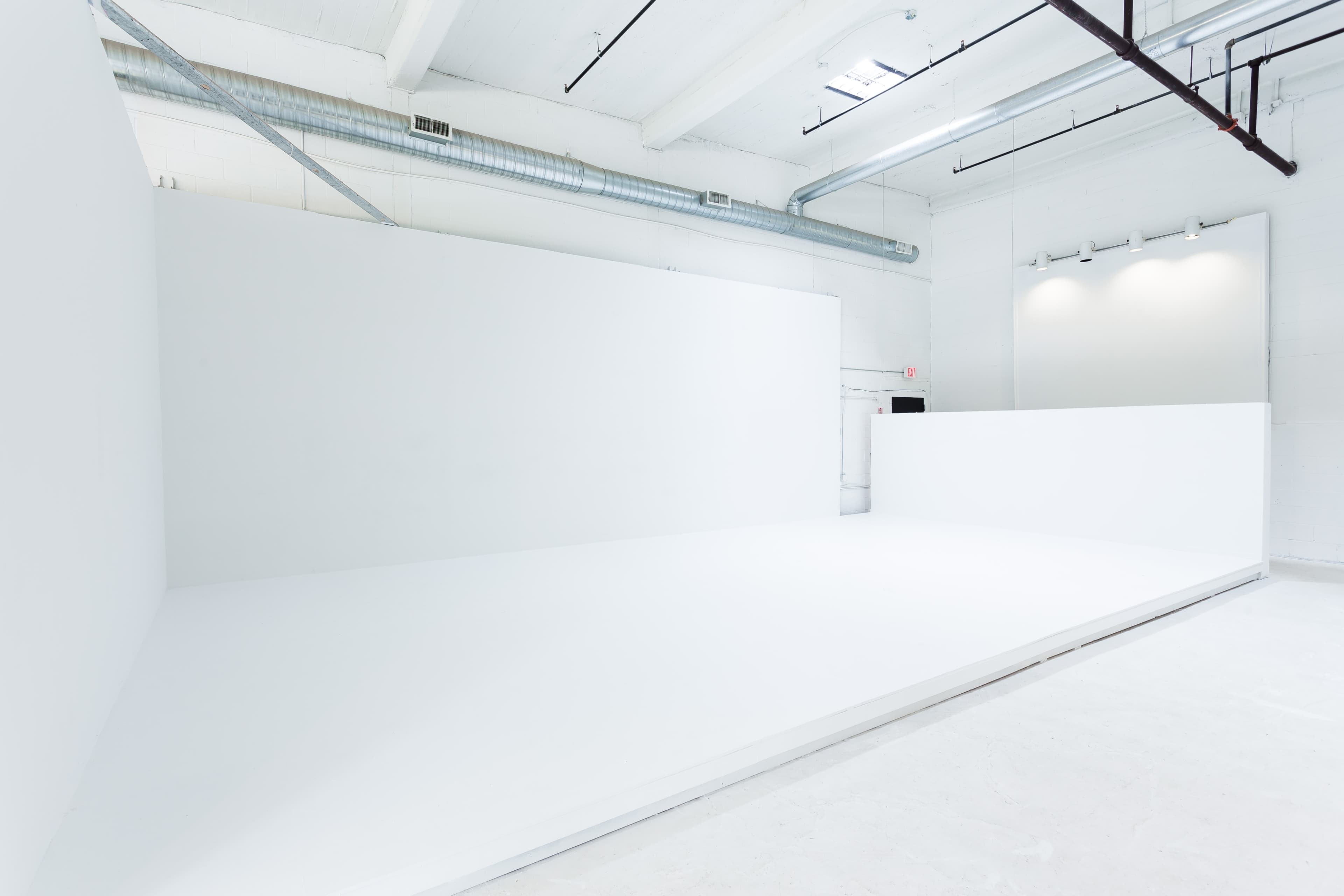 The image shows a spacious, empty studio with large white walls and a smooth white floor.