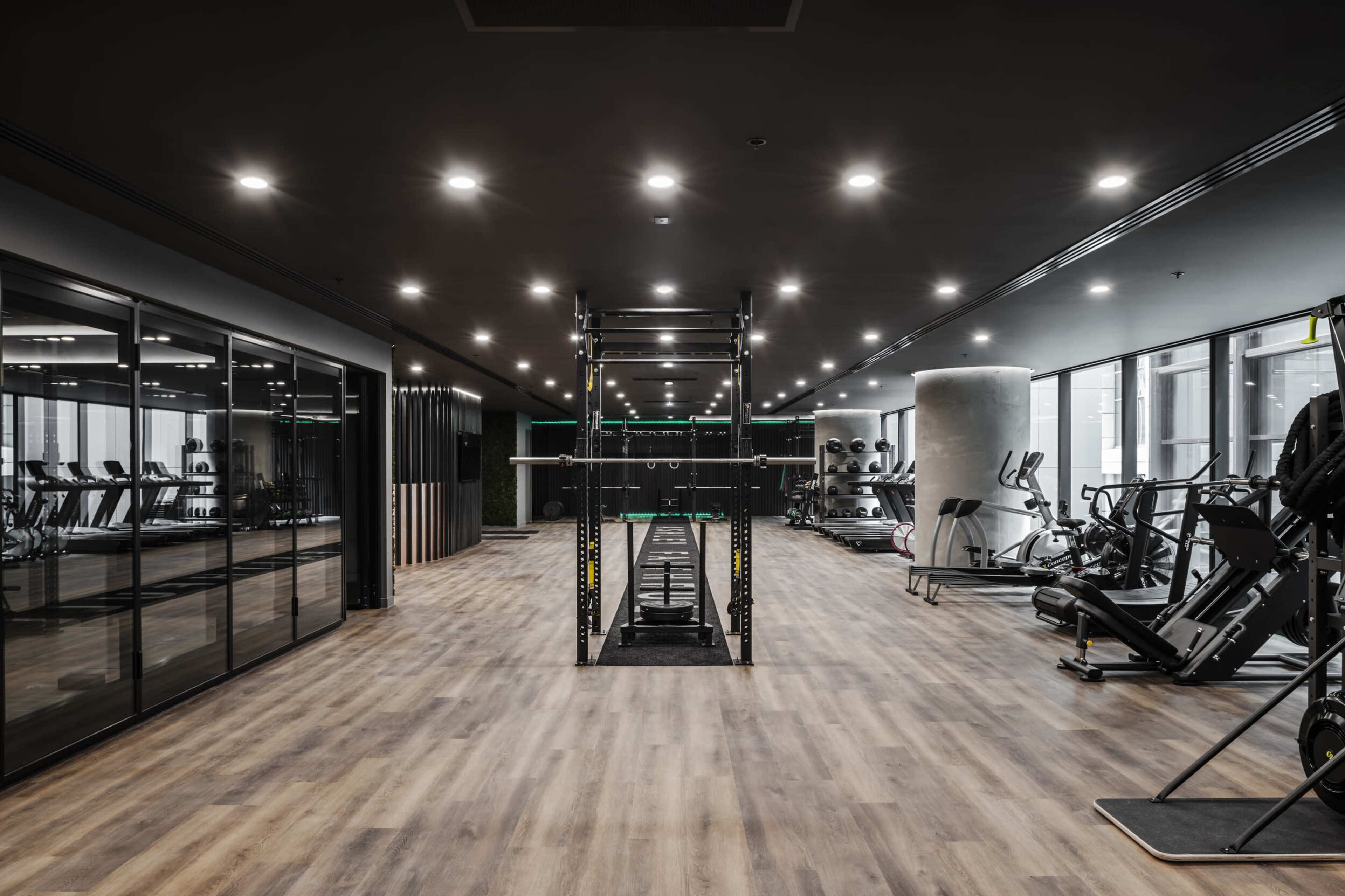 The image shows a modern gym interior featuring workout equipment, a lifting station, and large mirrors along the walls.
