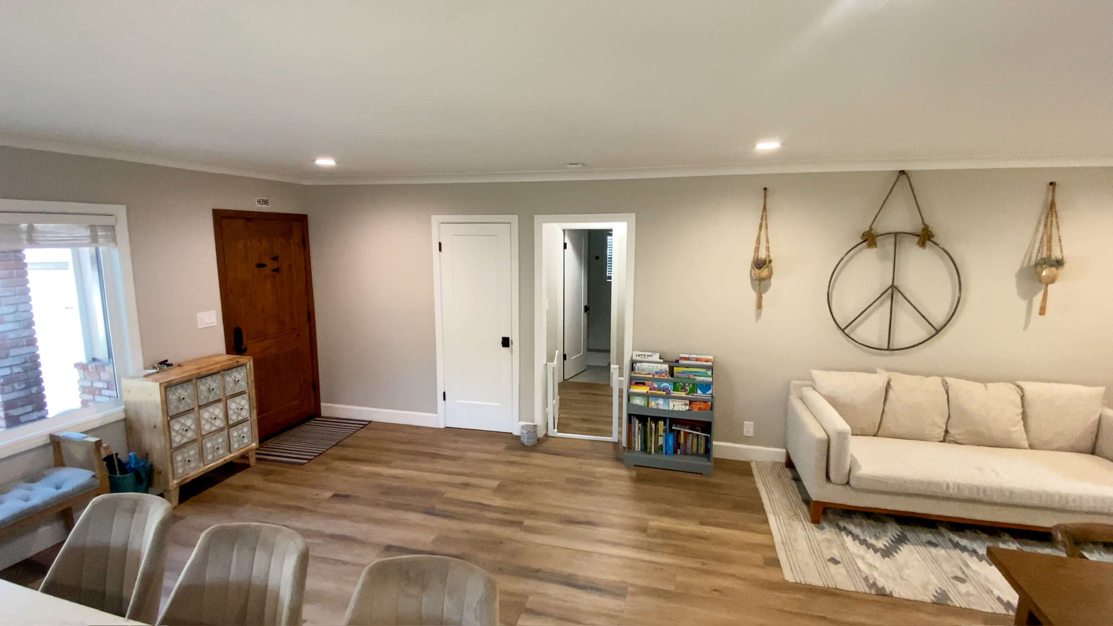 The image shows a living room featuring a couch, a peace sign wall decoration, a bookshelf, and a front door leading to a hallway.