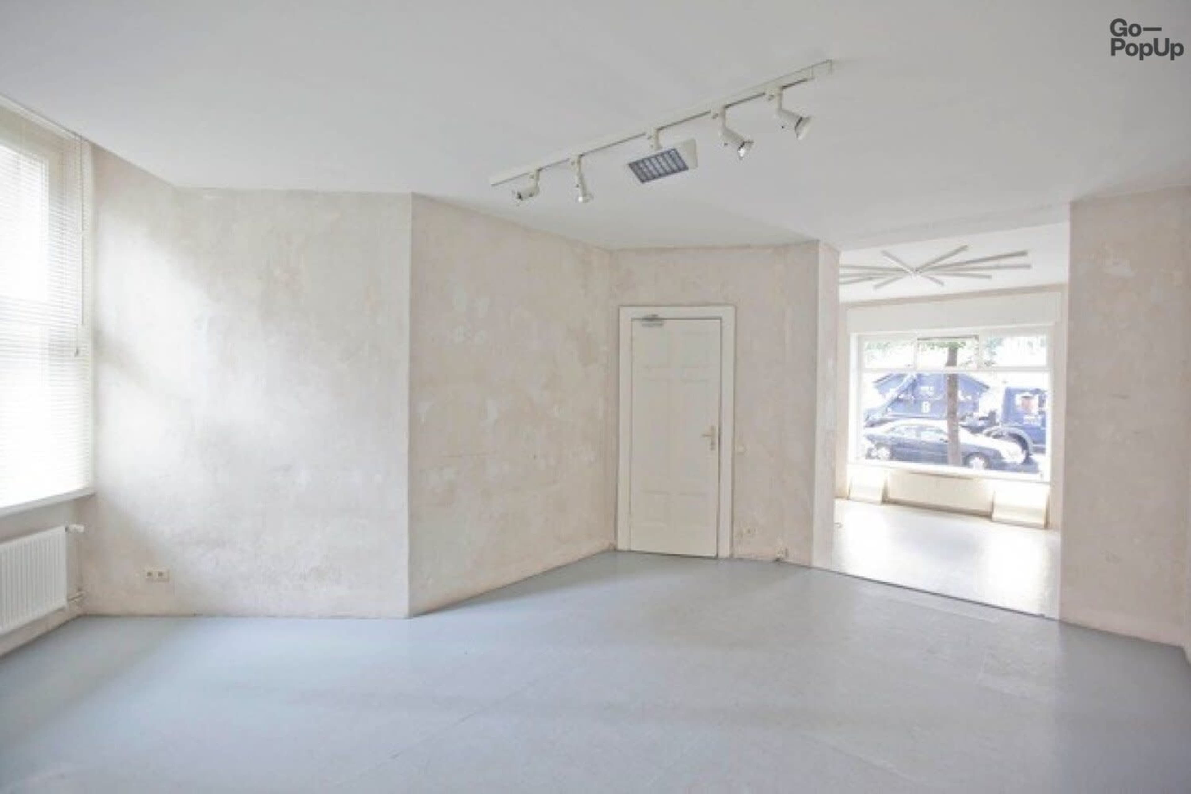 An empty room with light-colored walls, a simple door, and a large window facing the street.
