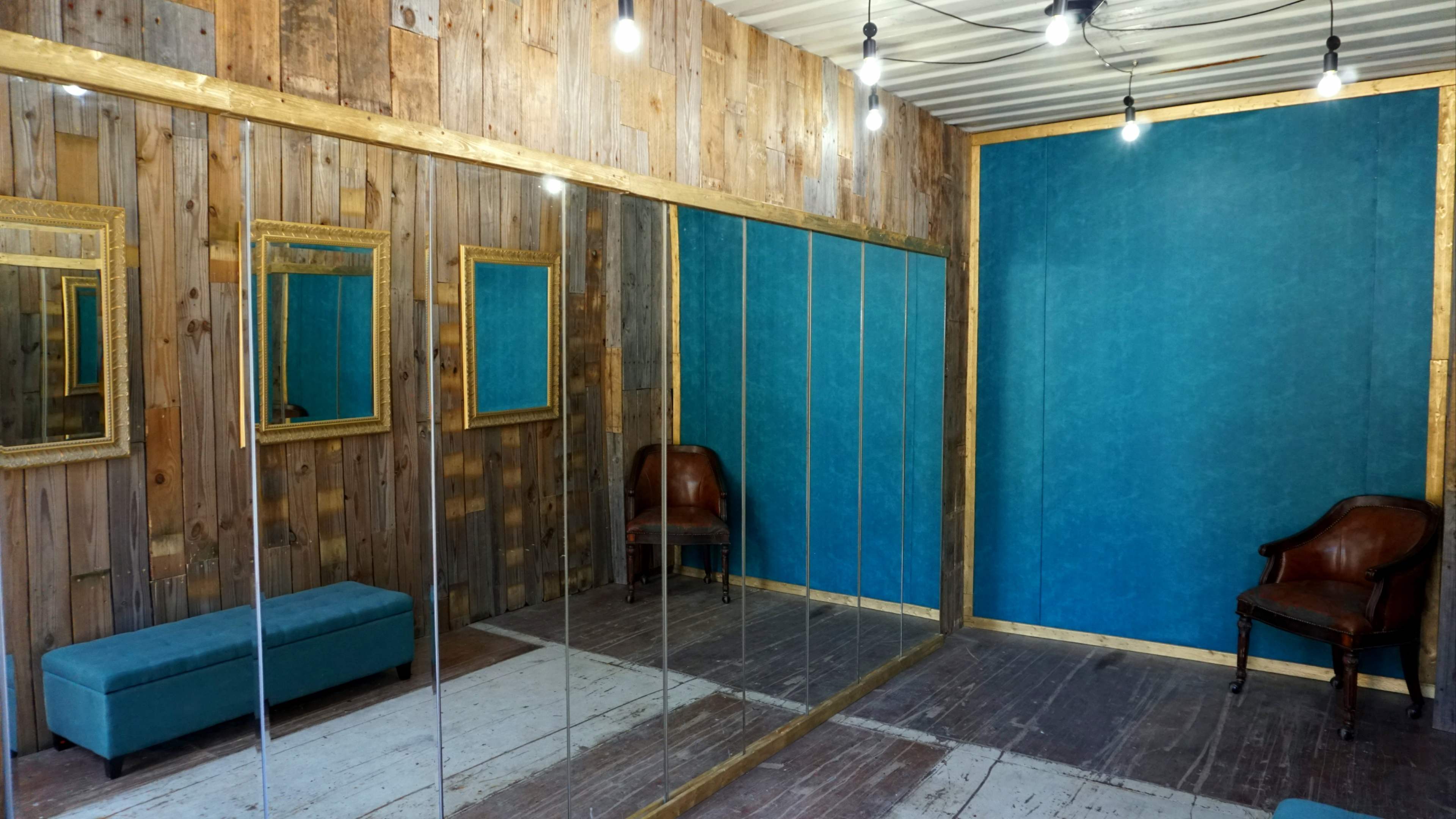 The image shows a room with wooden walls, two mirrors, a blue accent wall, a bench, and a brown chair.
