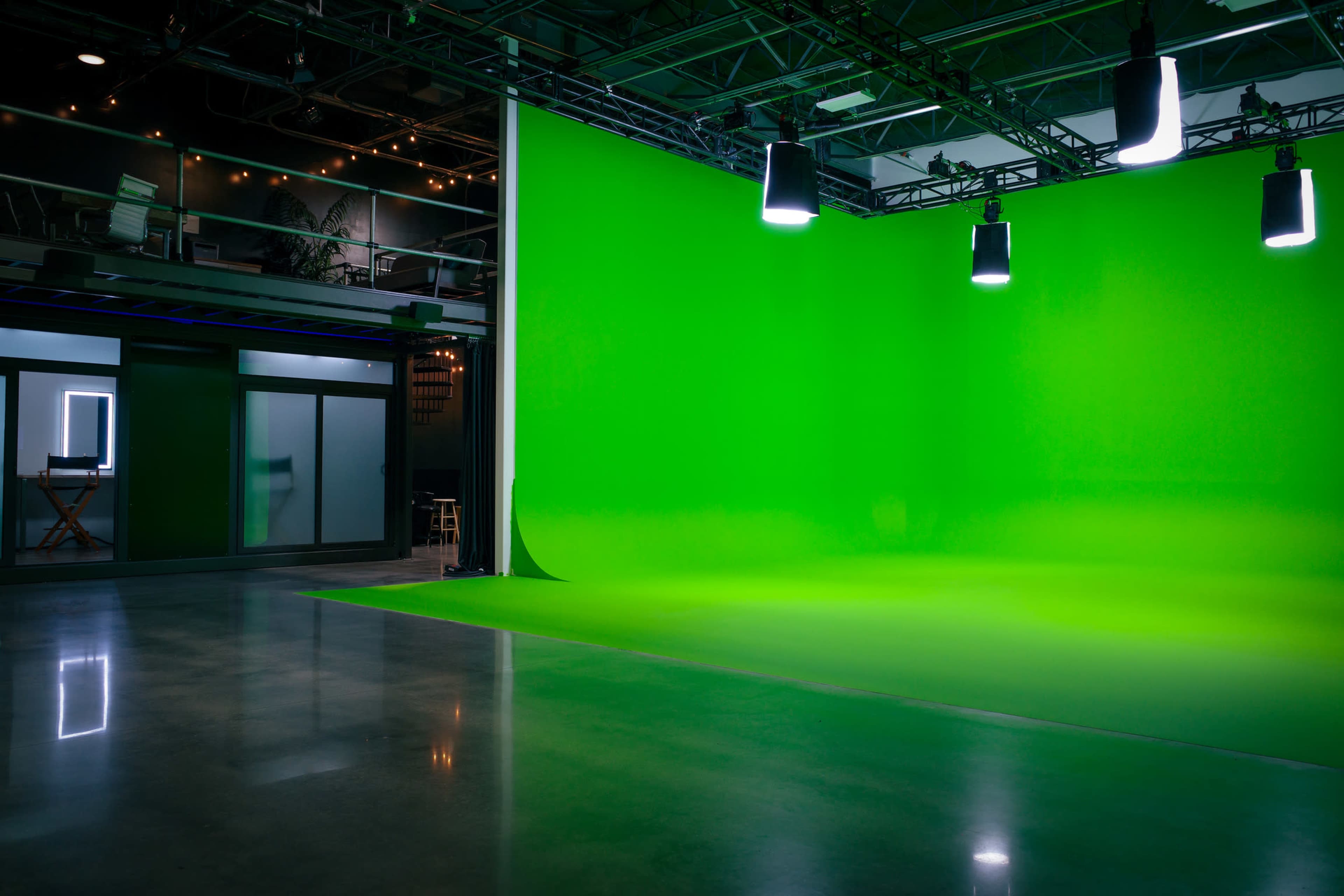 The image shows a modern studio with a bright green backdrop, illuminated by overhead lights, and polished concrete flooring.