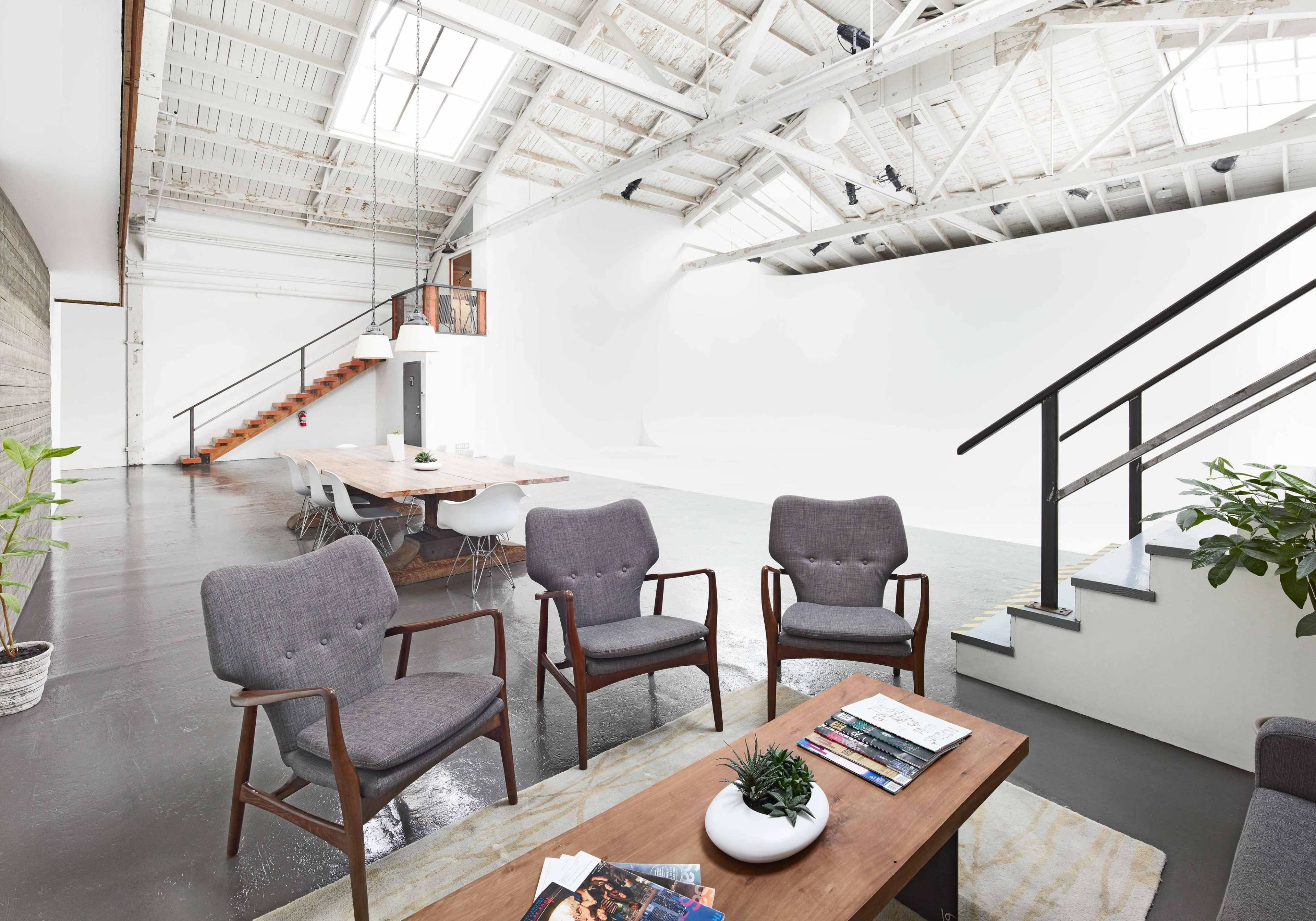 A spacious, modern interior featuring a long wooden dining table, gray chairs, and large windows allowing natural light to flood the room.