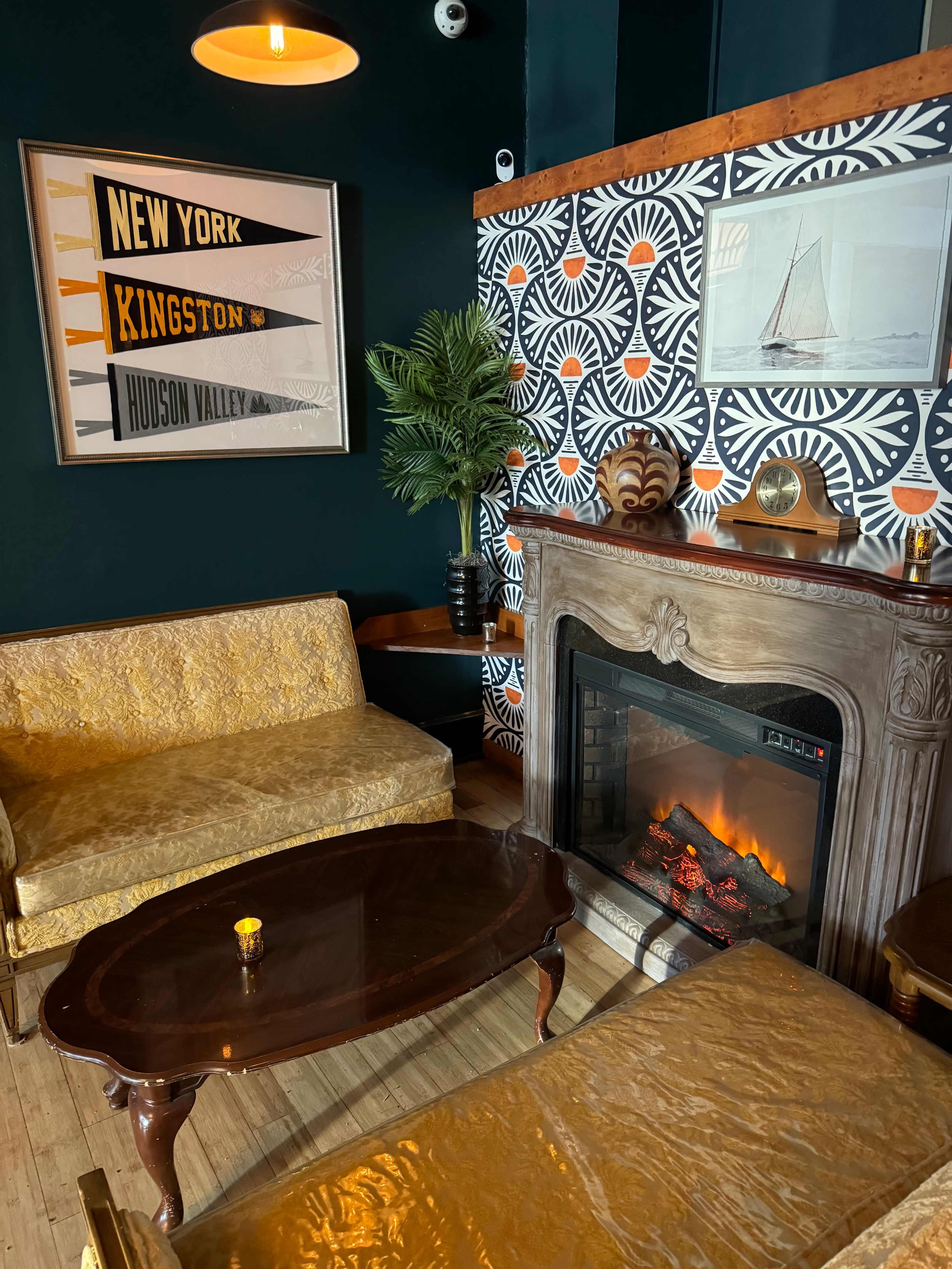 A cozy seating area with vintage-style yellow sofas, a wooden coffee table, and a decorative fireplace surrounded by patterned wallpaper.