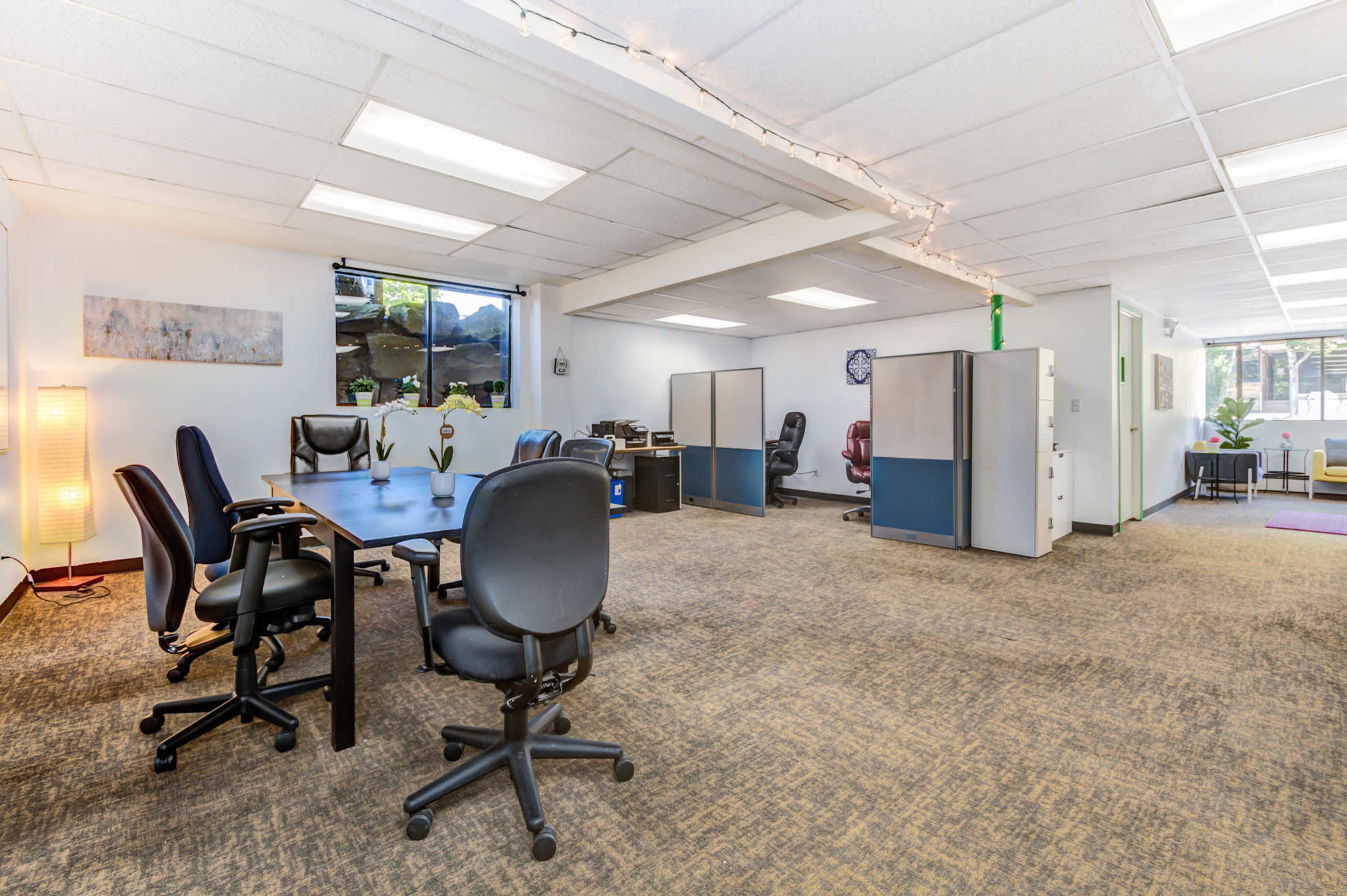 A spacious office area features several desks with chairs, partitions, and a light source, creating a functional workspace.
