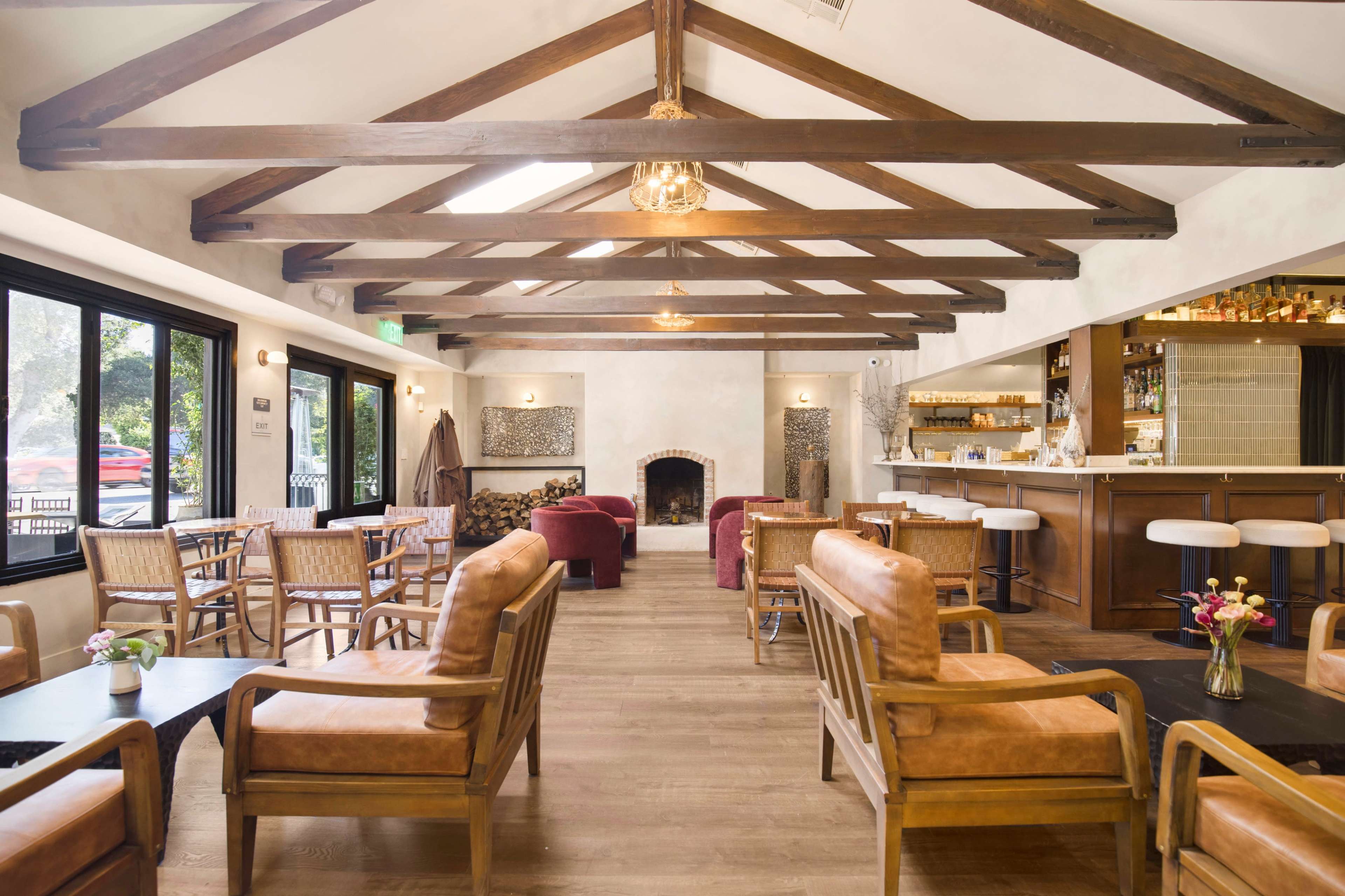 The image shows a spacious, cozy interior of a café featuring wooden beams, seating arrangements with leather chairs, and a bar area with a counter.