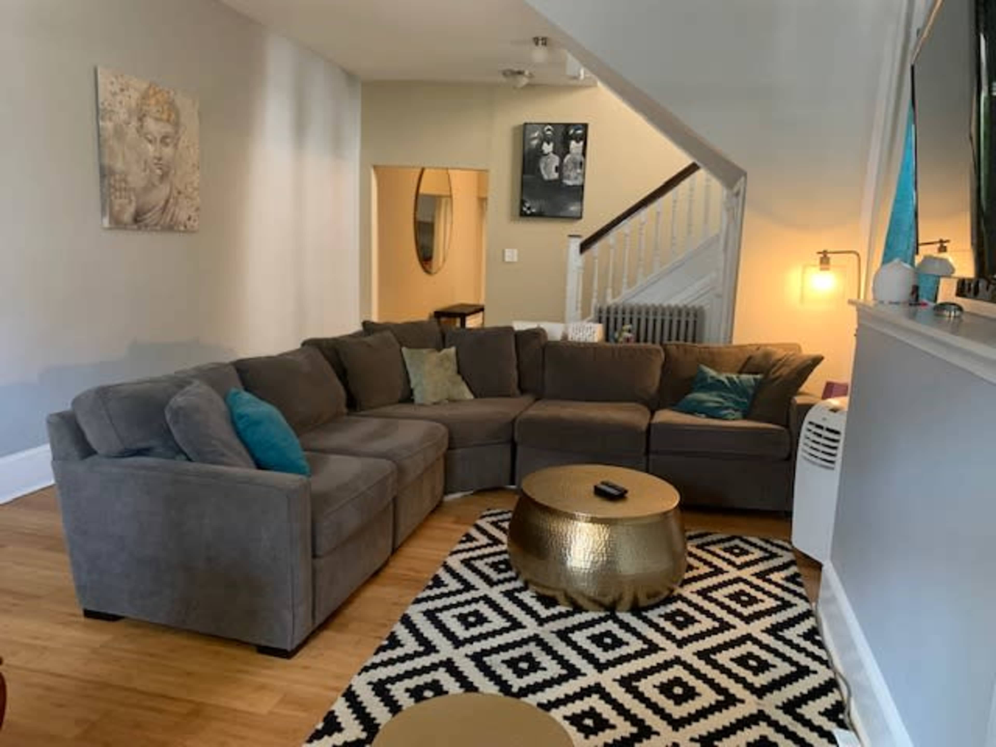 A living room featuring a large gray sectional sofa, a geometric black and white rug, and a round gold coffee table.