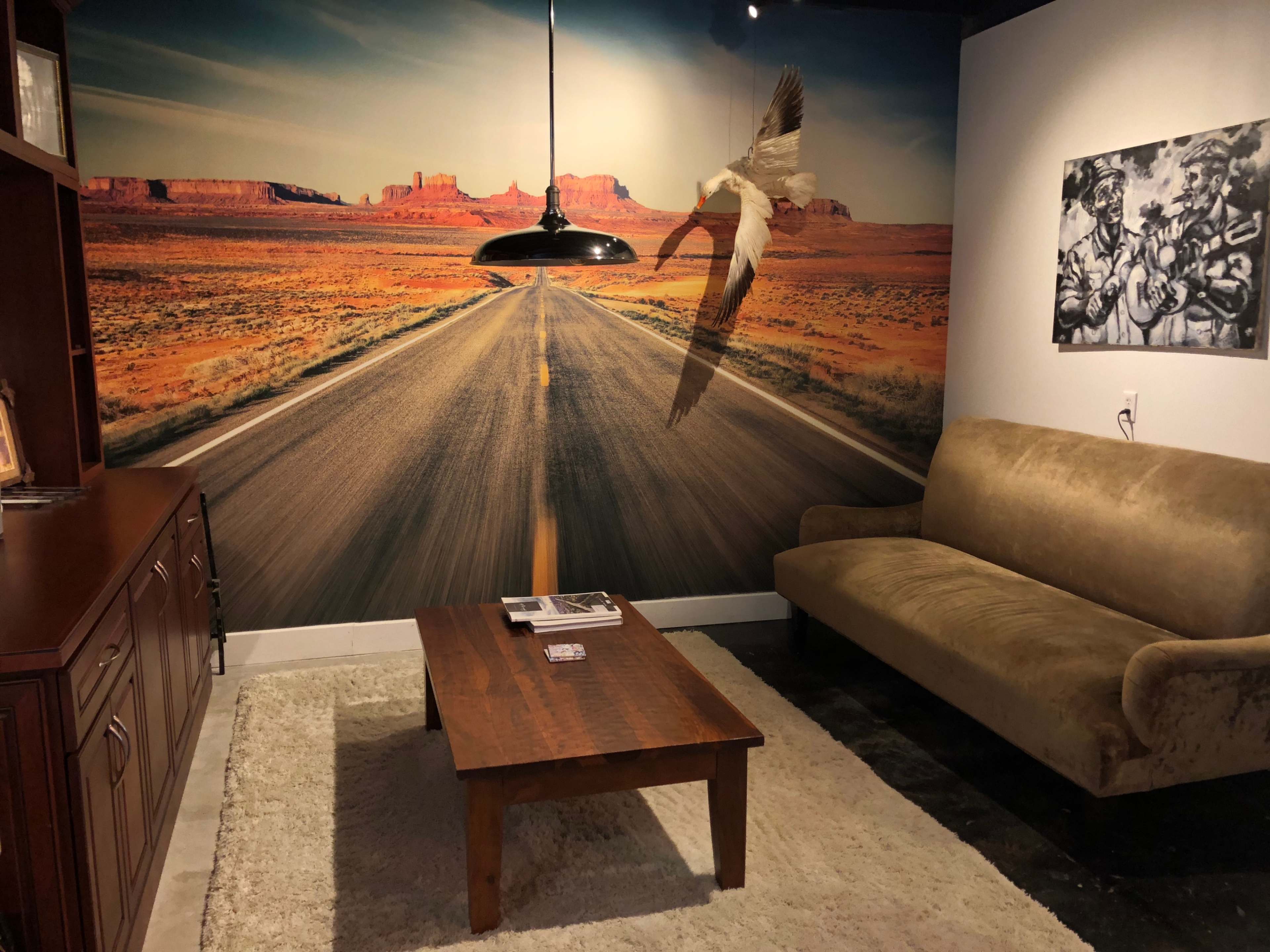 The image shows a room with a road mural on the wall, a brown sofa, a wooden coffee table, and a pendant light hanging above.