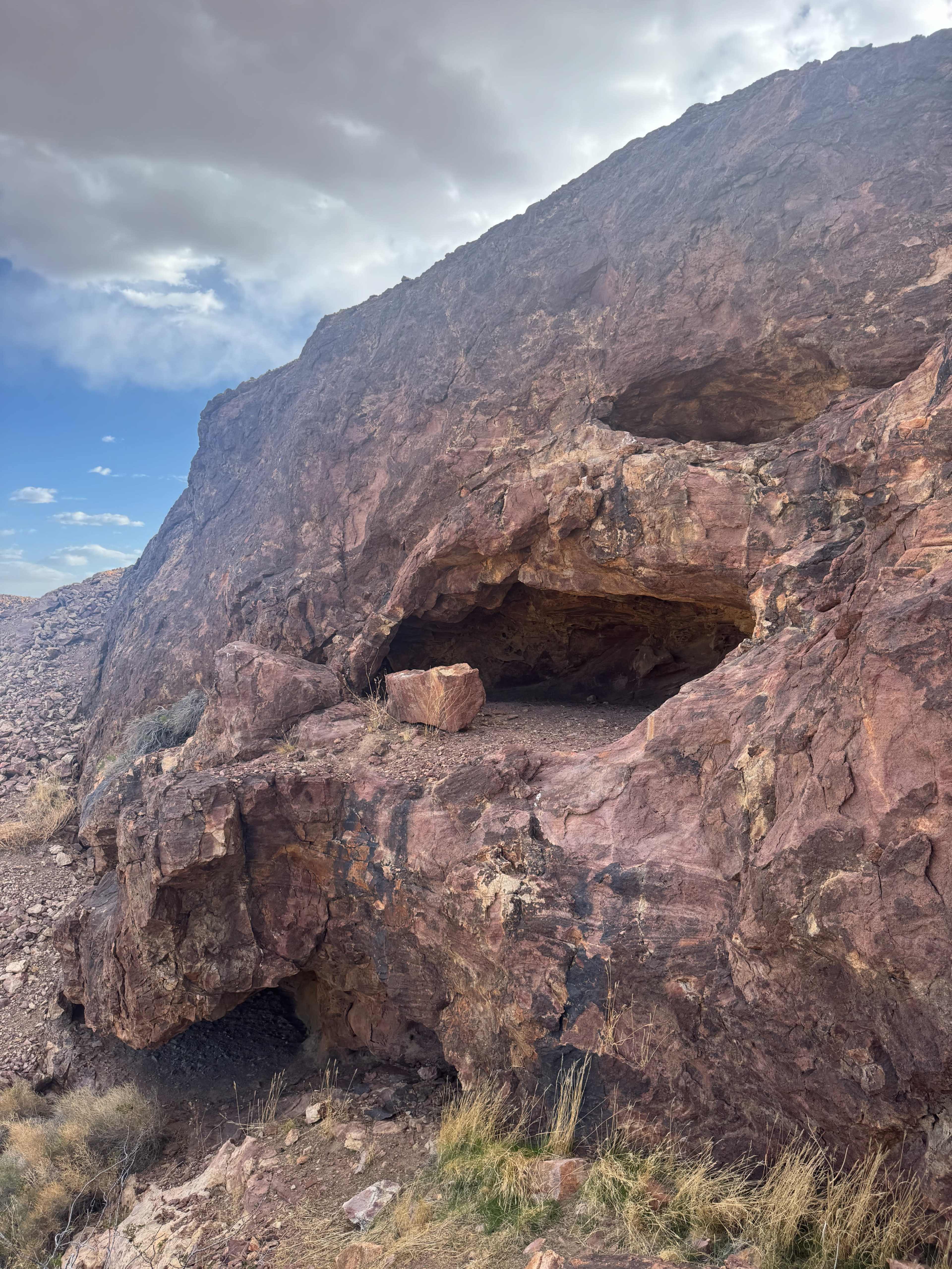 A rocky cliff features two natural recesses, with sparse vegetation at the base.