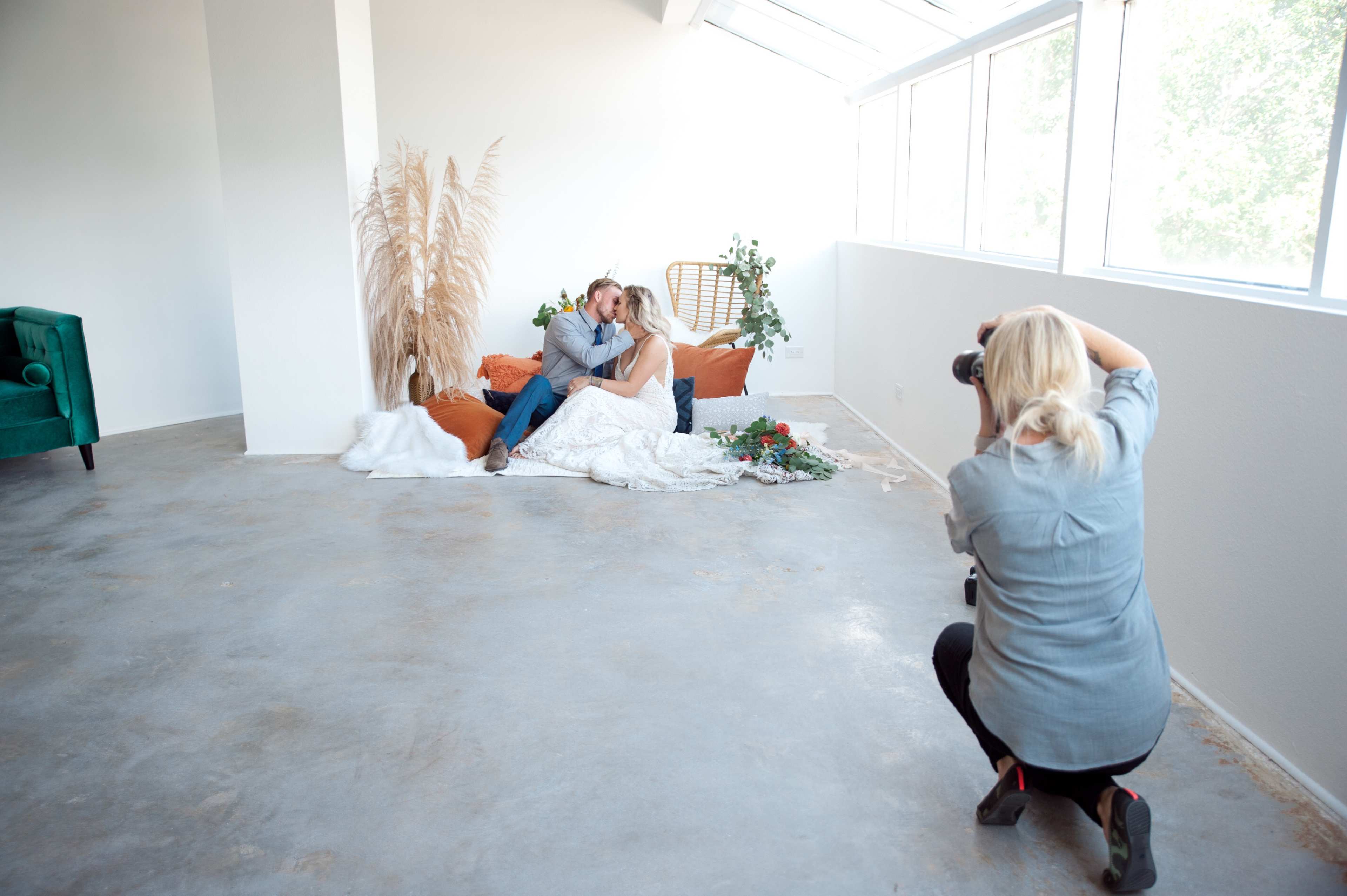 A photographer captures a couple posing on a couch surrounded by plants and decorative elements in a bright, airy room.