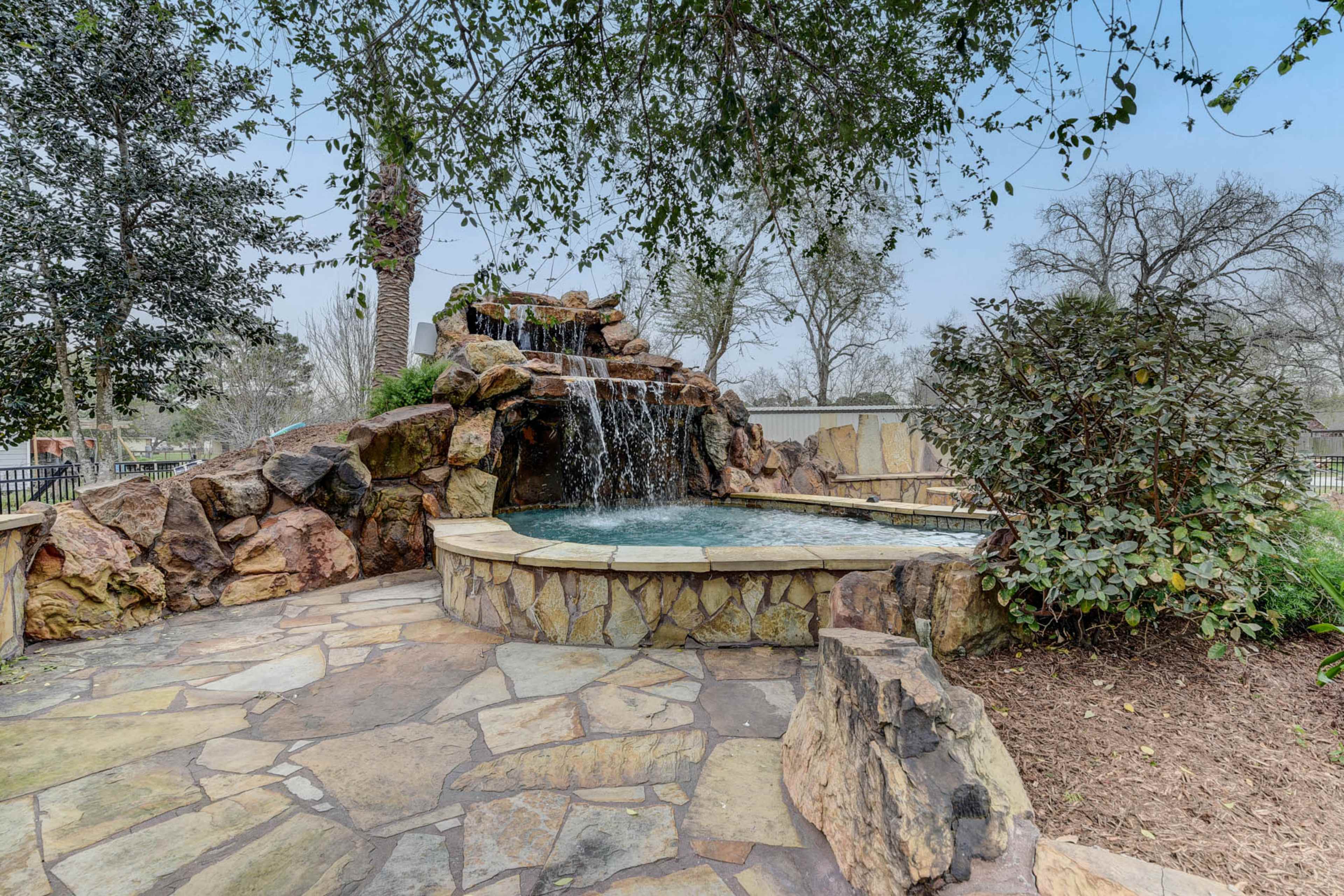 A stone waterfall cascades into a small pool surrounded by landscaped rocks and greenery.