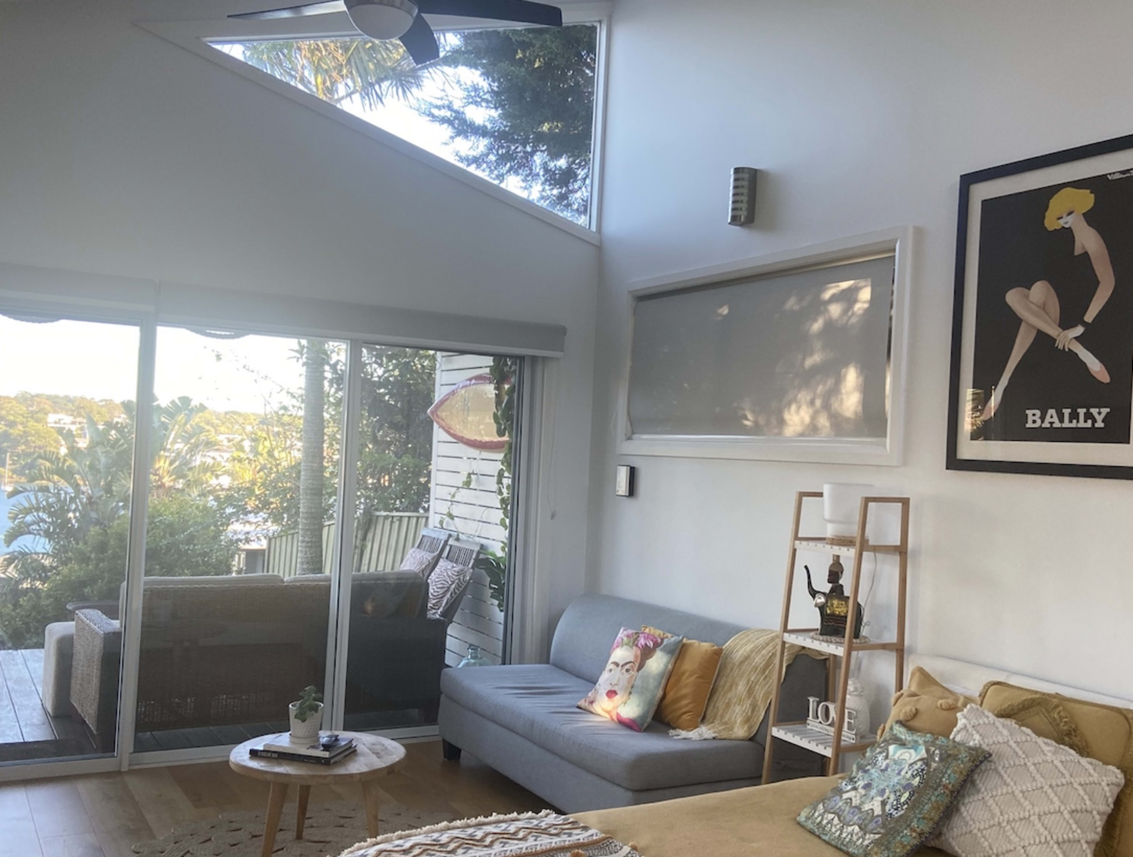 A modern living room with a gray sofa, a coffee table, and large windows revealing a view of greenery outside.