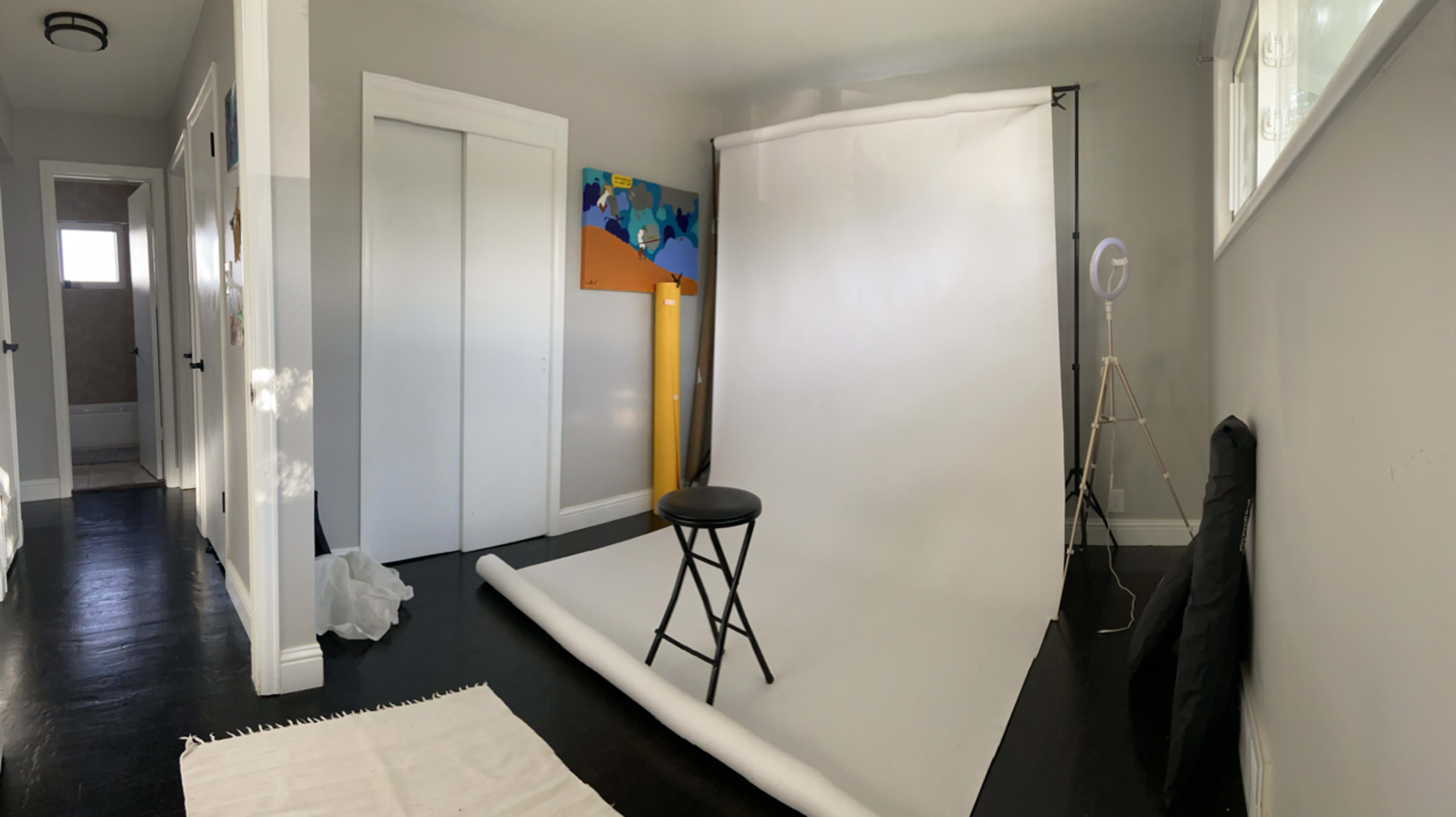 A photography studio featuring a white backdrop, a black stool, and colorful artwork on the wall.