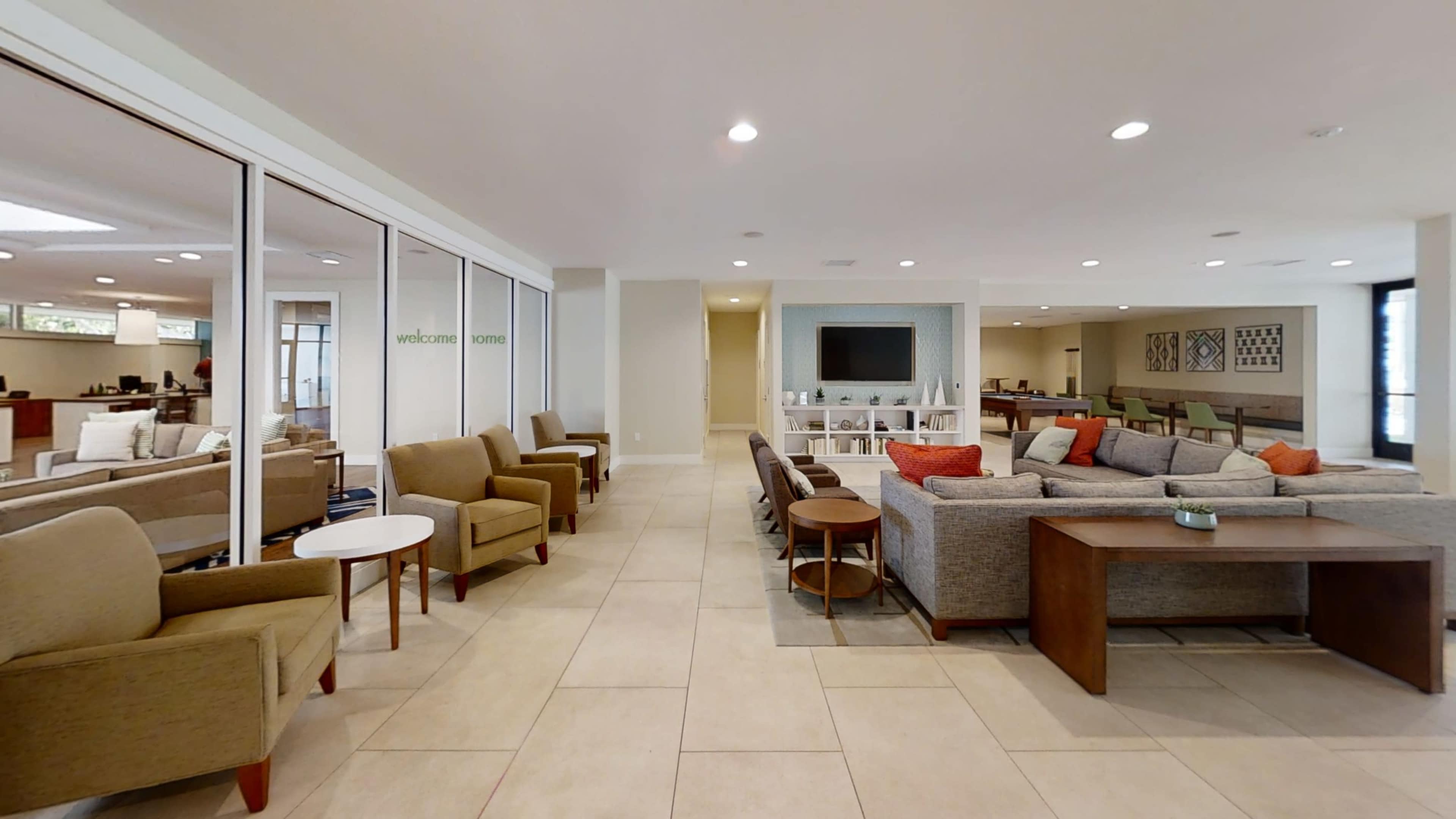 A spacious, modern common area with multiple seating arrangements, including sofas and armchairs, arranged around coffee tables.
