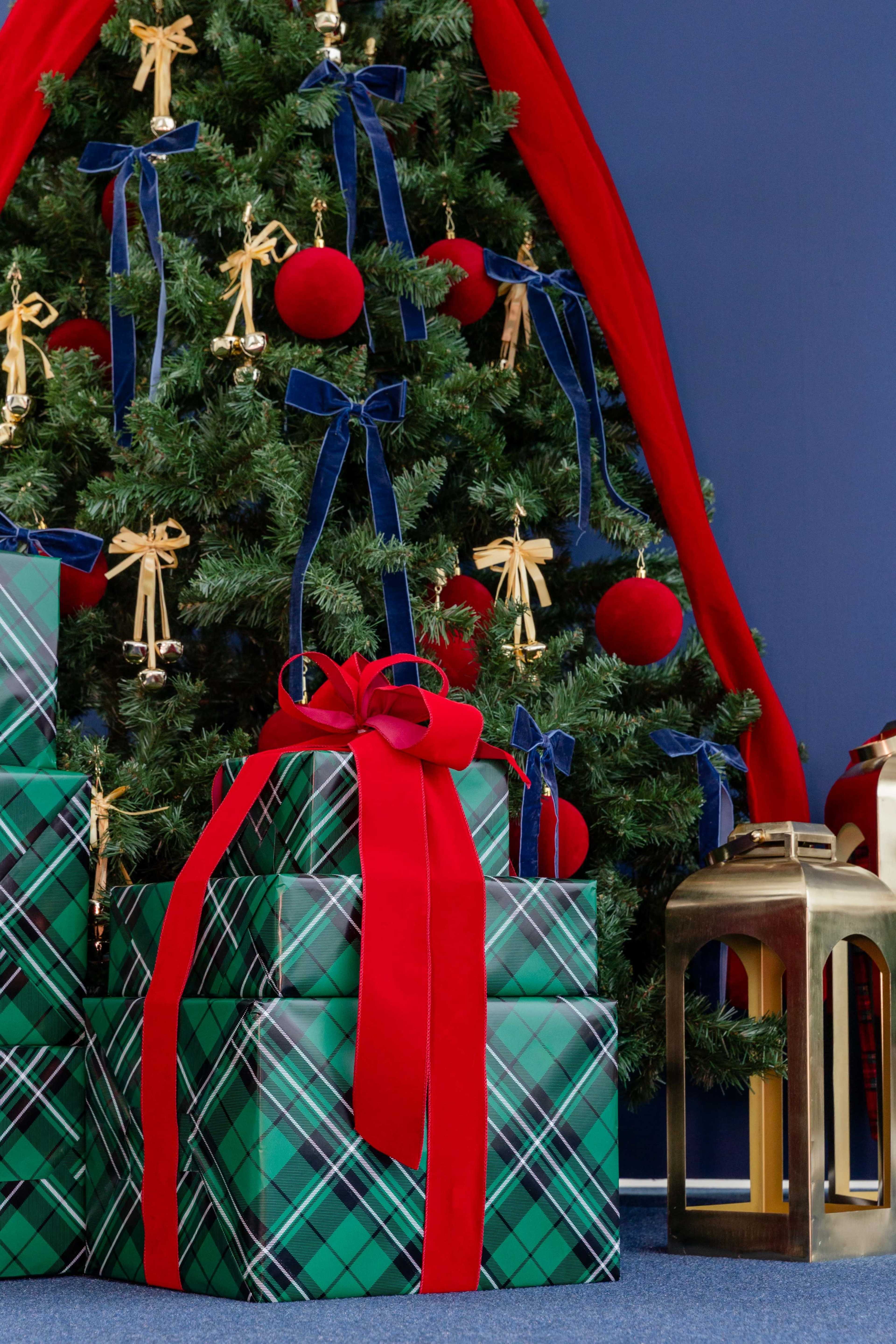 A decorated Christmas tree with gold ornaments and red ribbons stands beside neatly wrapped green plaid presents tied with red bows.