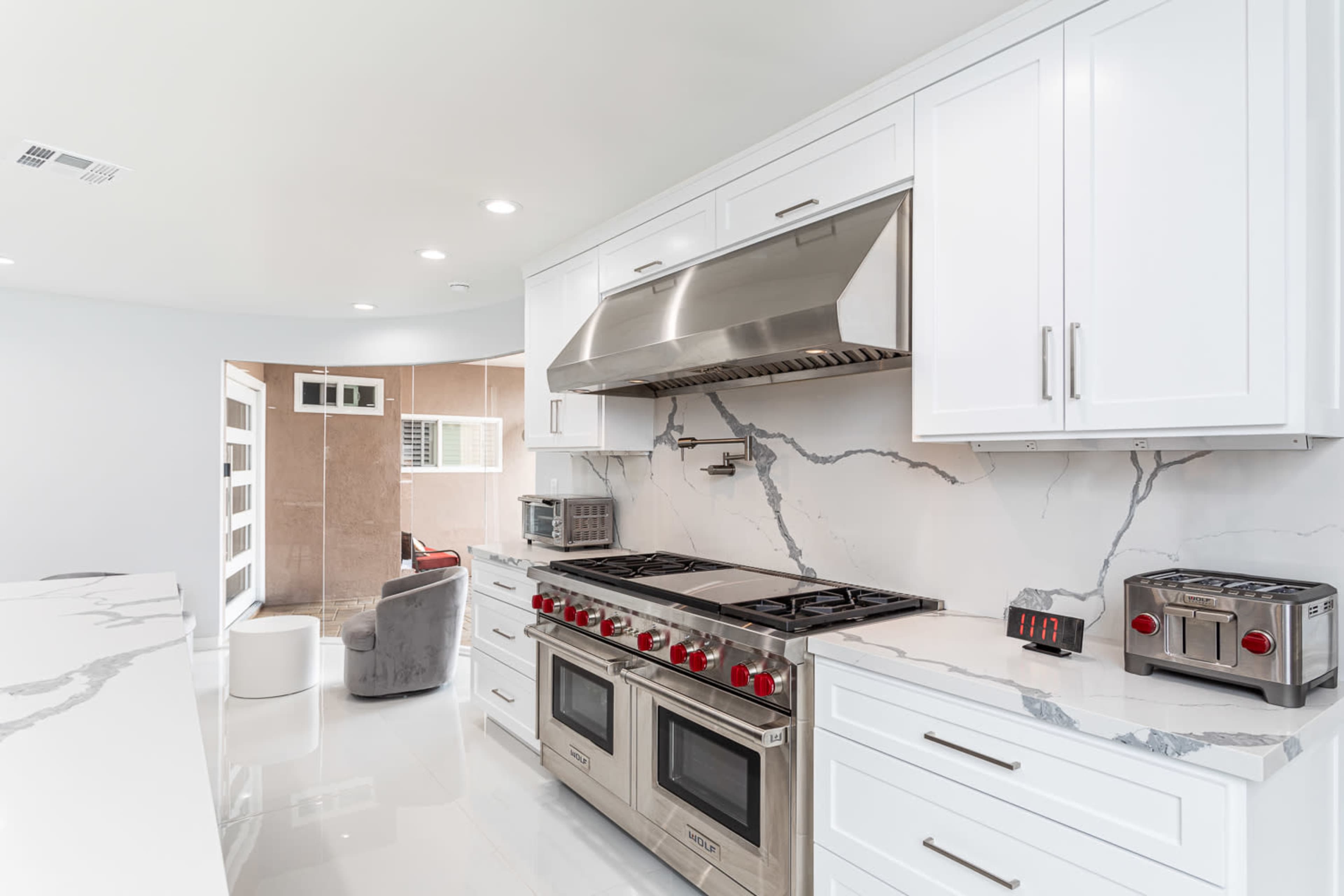 A modern kitchen featuring white cabinetry, a stainless steel range with red knobs, and a marble countertop.