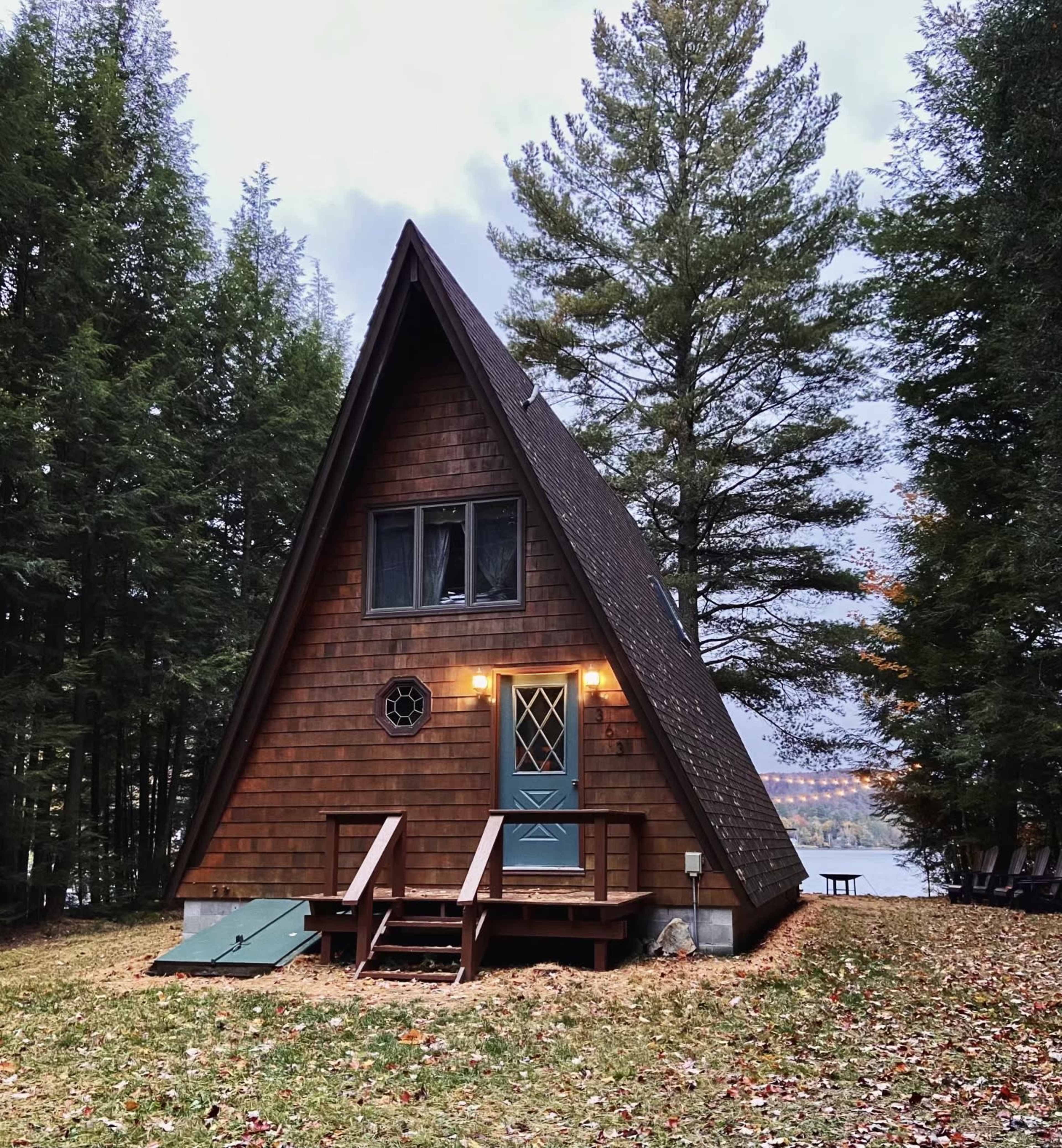 The image shows a wooden A-frame cabin set among tall trees near a lake.