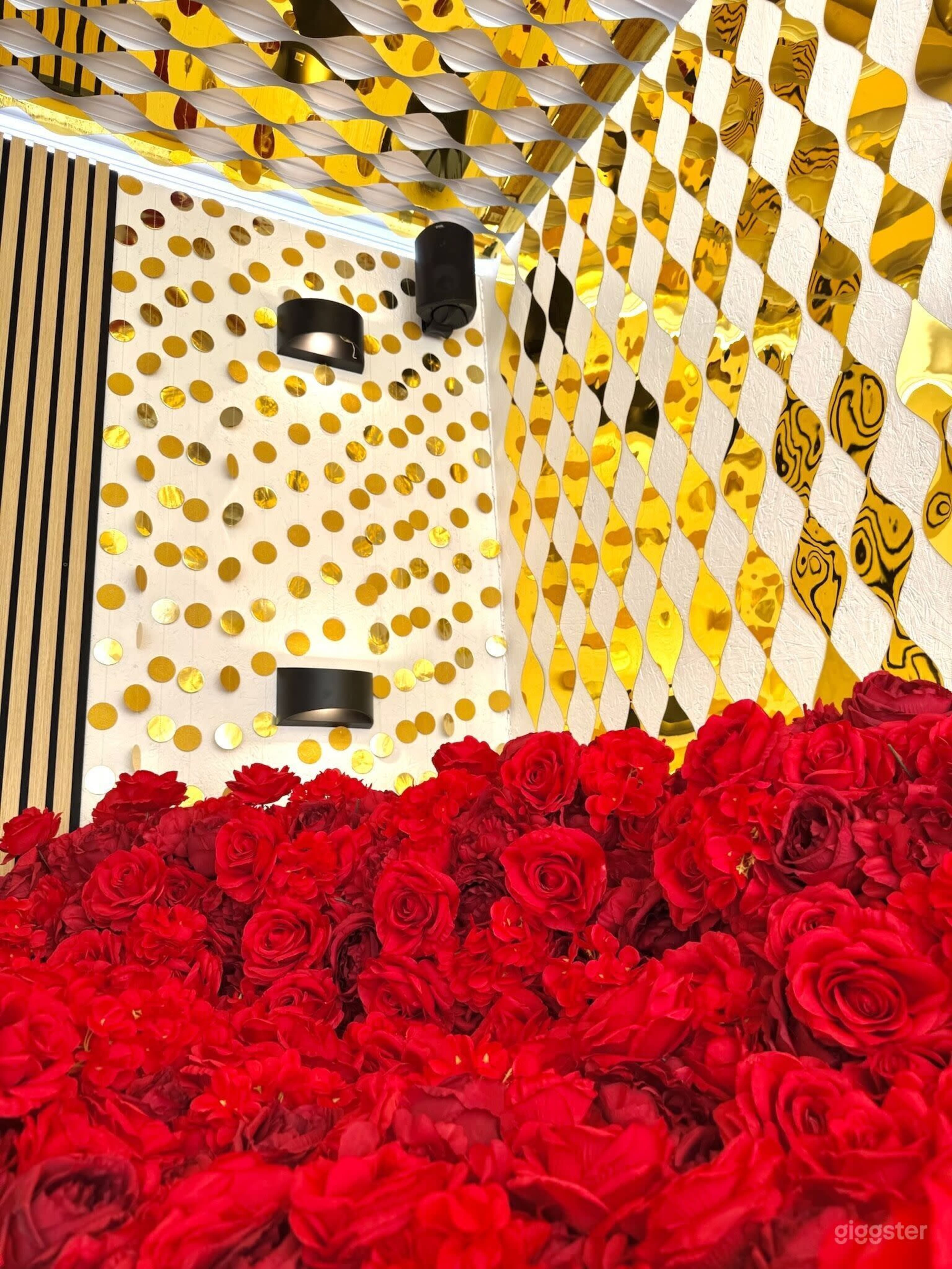 The image features a room filled with vibrant red roses and a gold, reflective wall adorned with circular patterns.